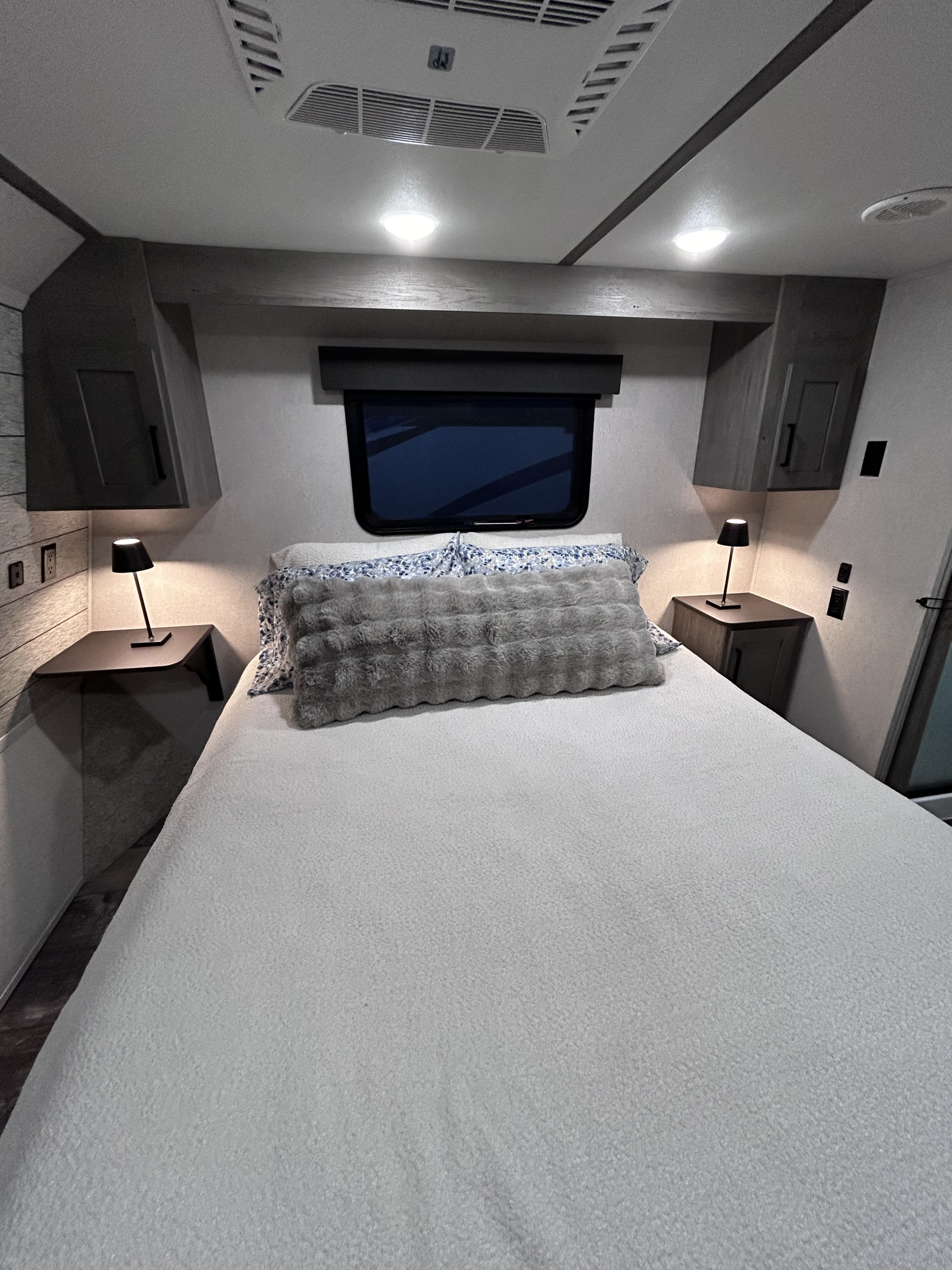 Comfortable RV rental bedroom featuring a cozy bed, nightstands, and overhead storage, ideal for travelers.. Keystone Raptor 2021