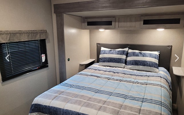 RV rental bedroom with a full bed, striped comforter, bedside shelves, and overhead cabinets for a comfortable stay.. Coachman Catalina 343BHTSLE 2021