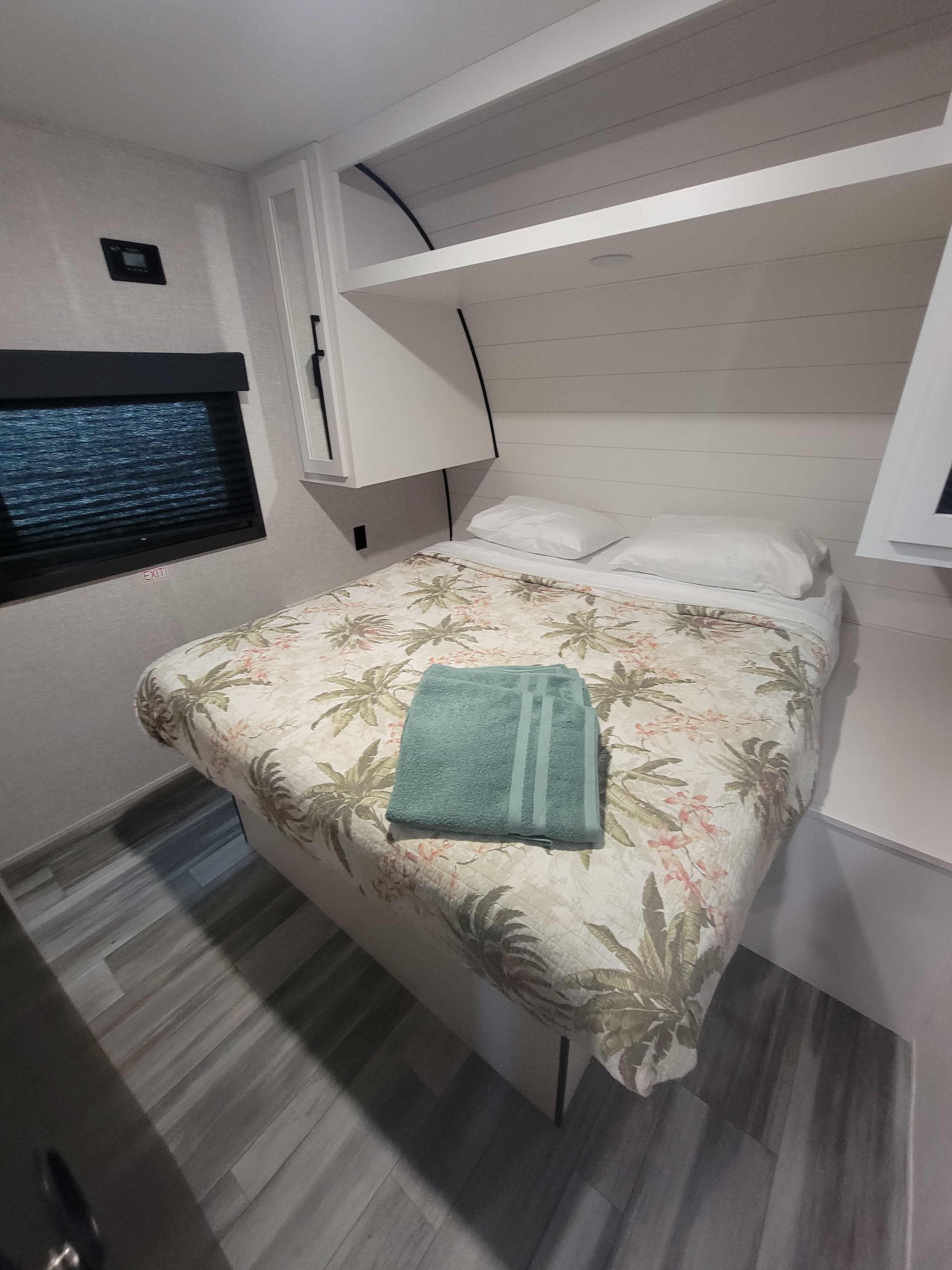 Cozy RV rental bedroom with tropical bedspread, white pillows, and overhead cabinets. Ideal interior for a comfortable getaway.. Starcraft Autunm Ridge 26bh 2024