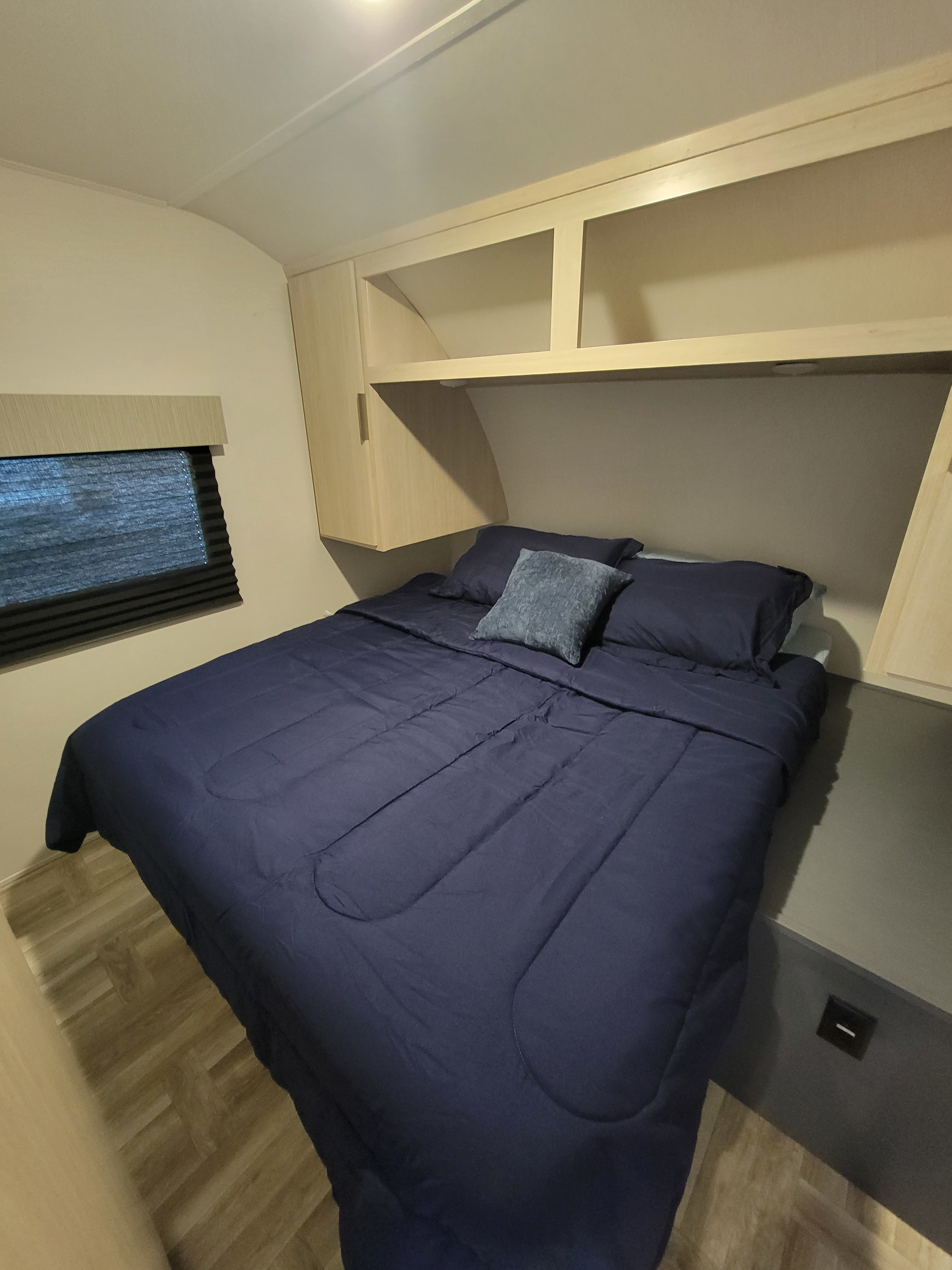 Cozy RV rental bedroom featuring a large bed with blue bedding, overhead storage, and a window for comfort on your travels.. Prime Time Tracer 2700BHSLE 2024