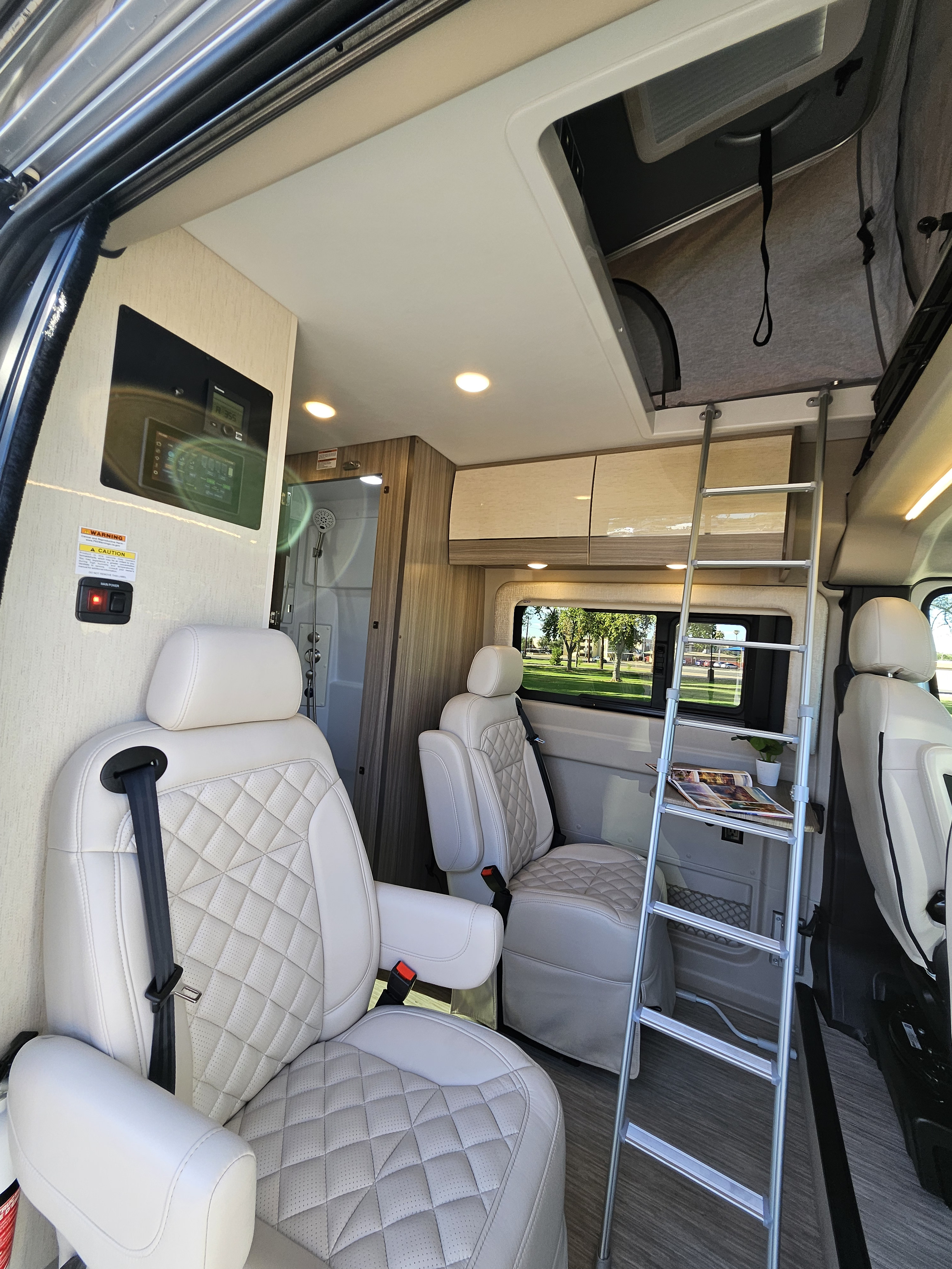 Spacious RV rental interior featuring plush, quilted cream seats, a ladder to an overhead bunk, and built-in amenities.. Entegra Coach Ethos 2024