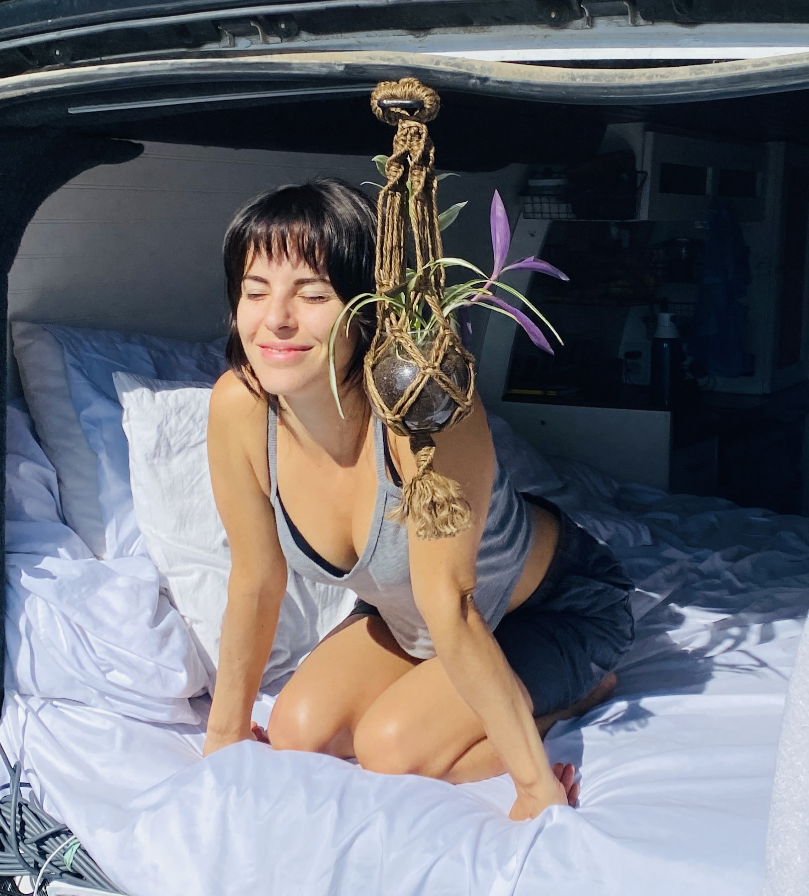 Woman smiles in her comfortable RV rental bed, bathed in sunlight. A peaceful van life moment.. Chevrolet Express 3500 2012