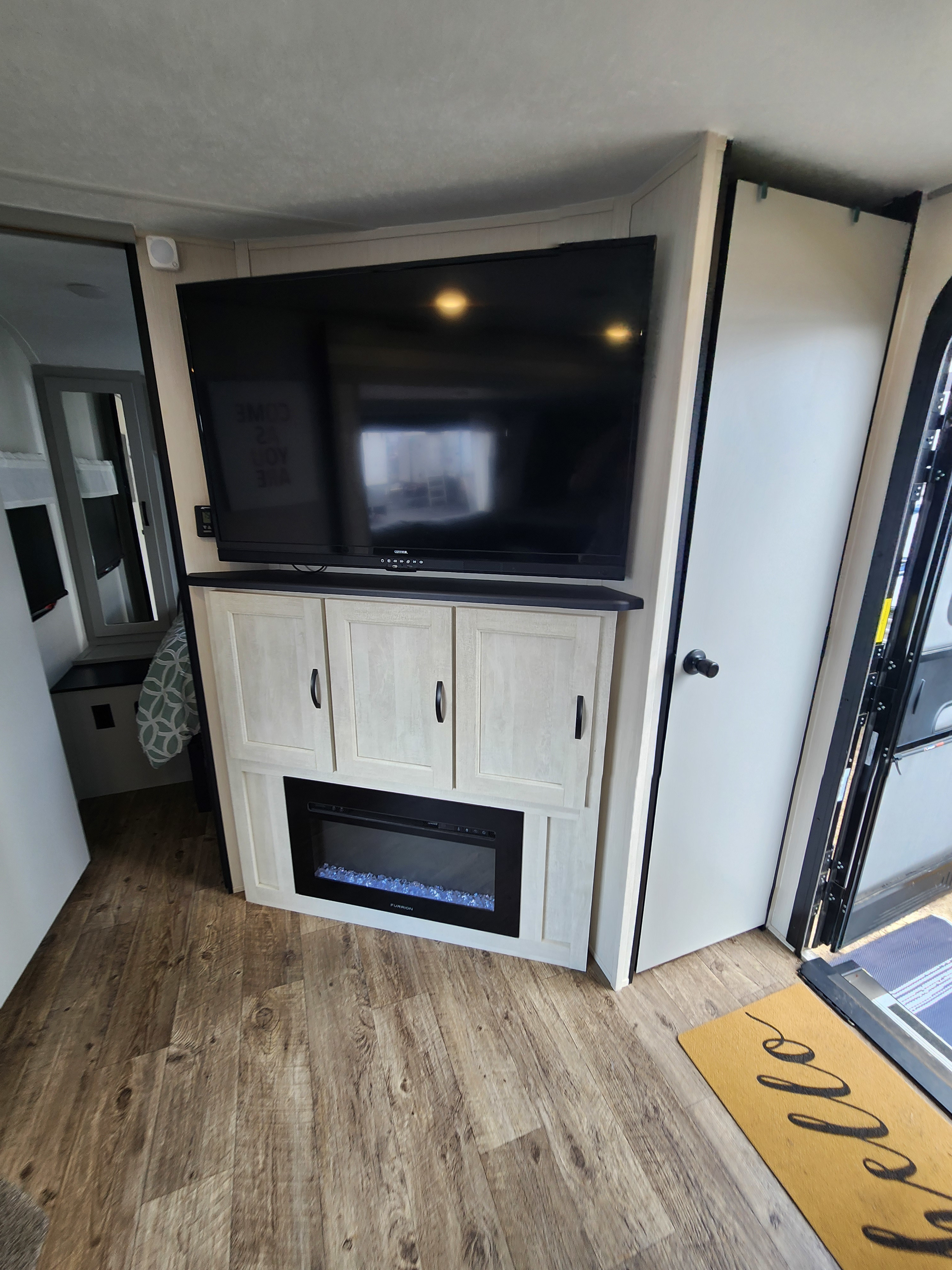 Modern RV rental living area featuring a large TV, built-in electric fireplace, and stylish wood-look flooring.. Forest River Vibe 2022