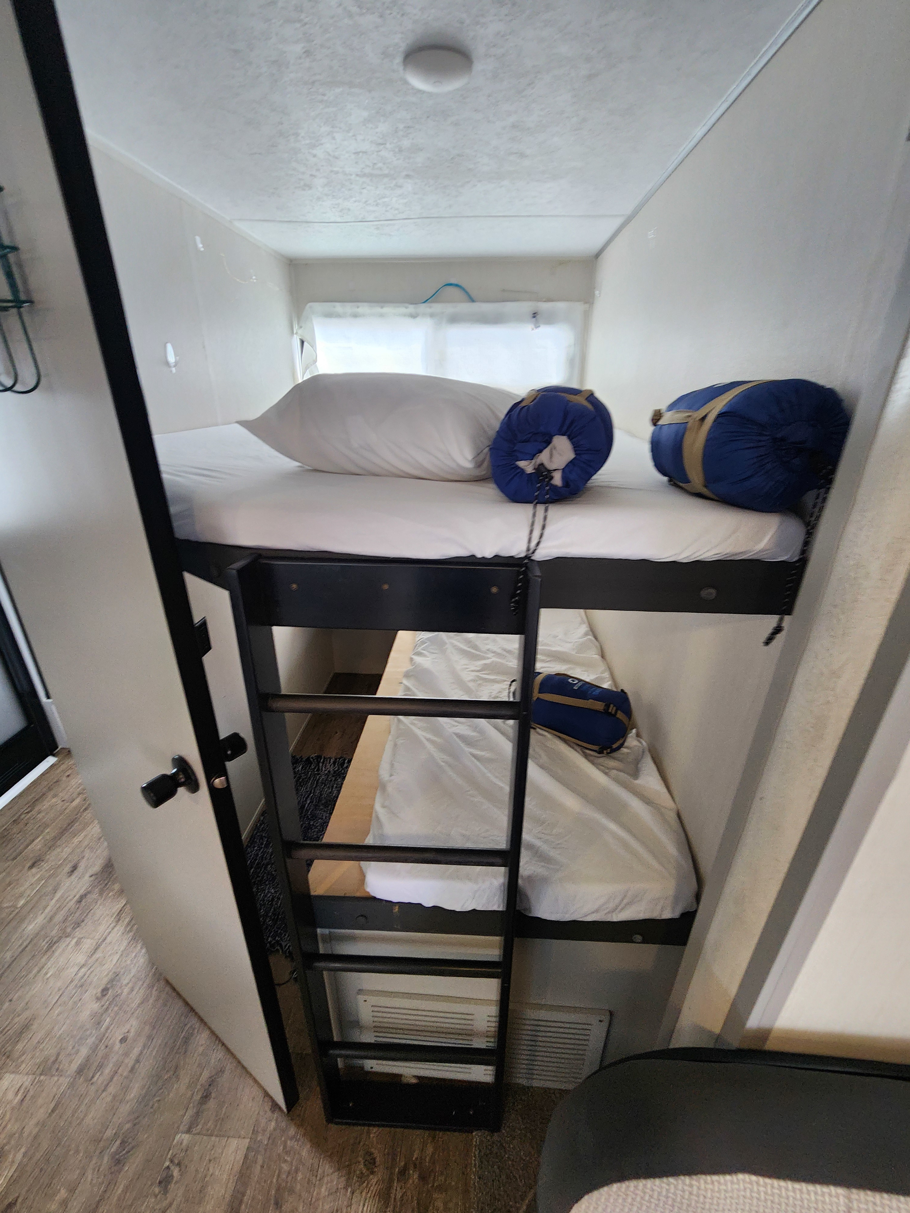 Cozy bunk beds in an RV rental, featuring two sleeping spaces with white sheets, pillows, and rolled sleeping bags. Ladder for top bunk.. Forest River Vibe 2022