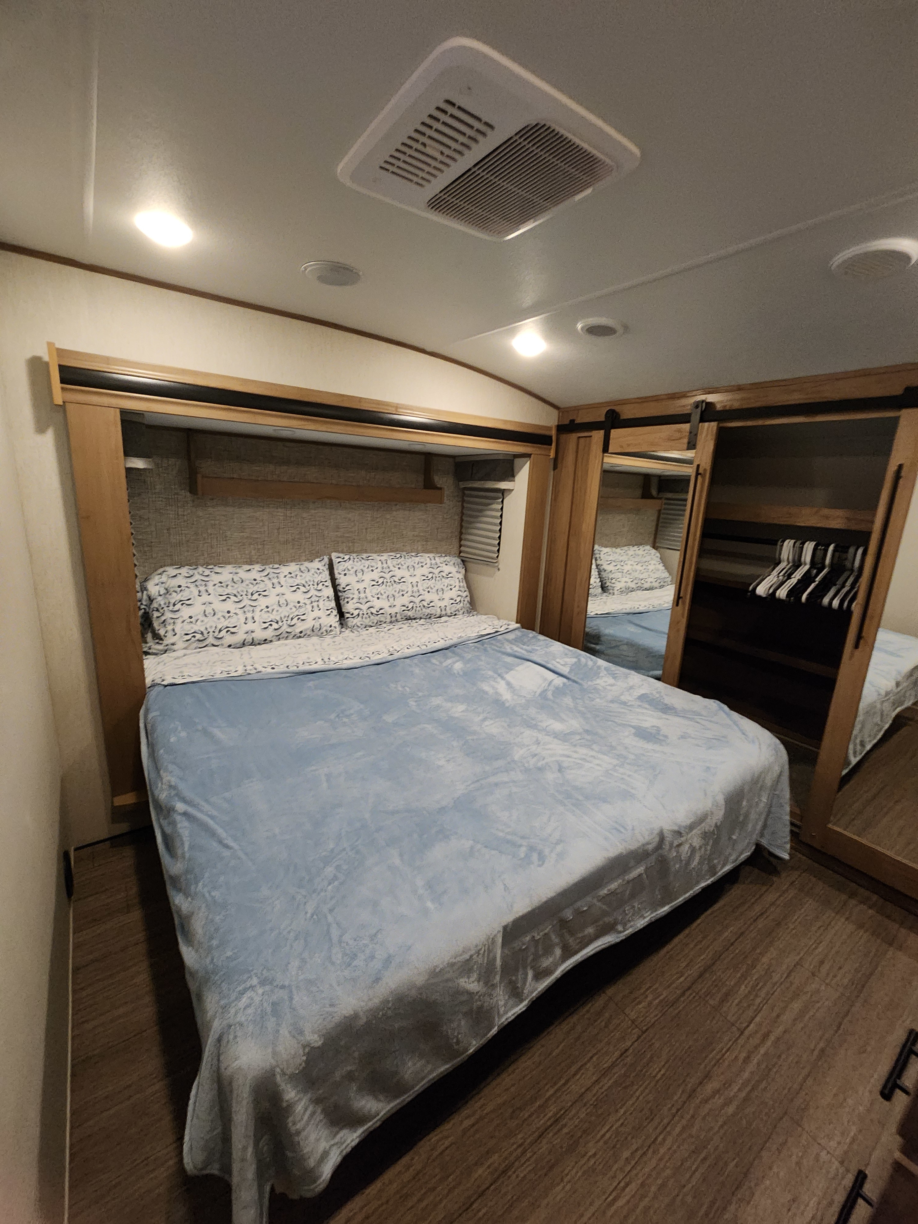 Inside an RV rental, a well-appointed bedroom featuring a large bed, mirrored closet, and overhead AC vent.. Forest River Sabre 2023