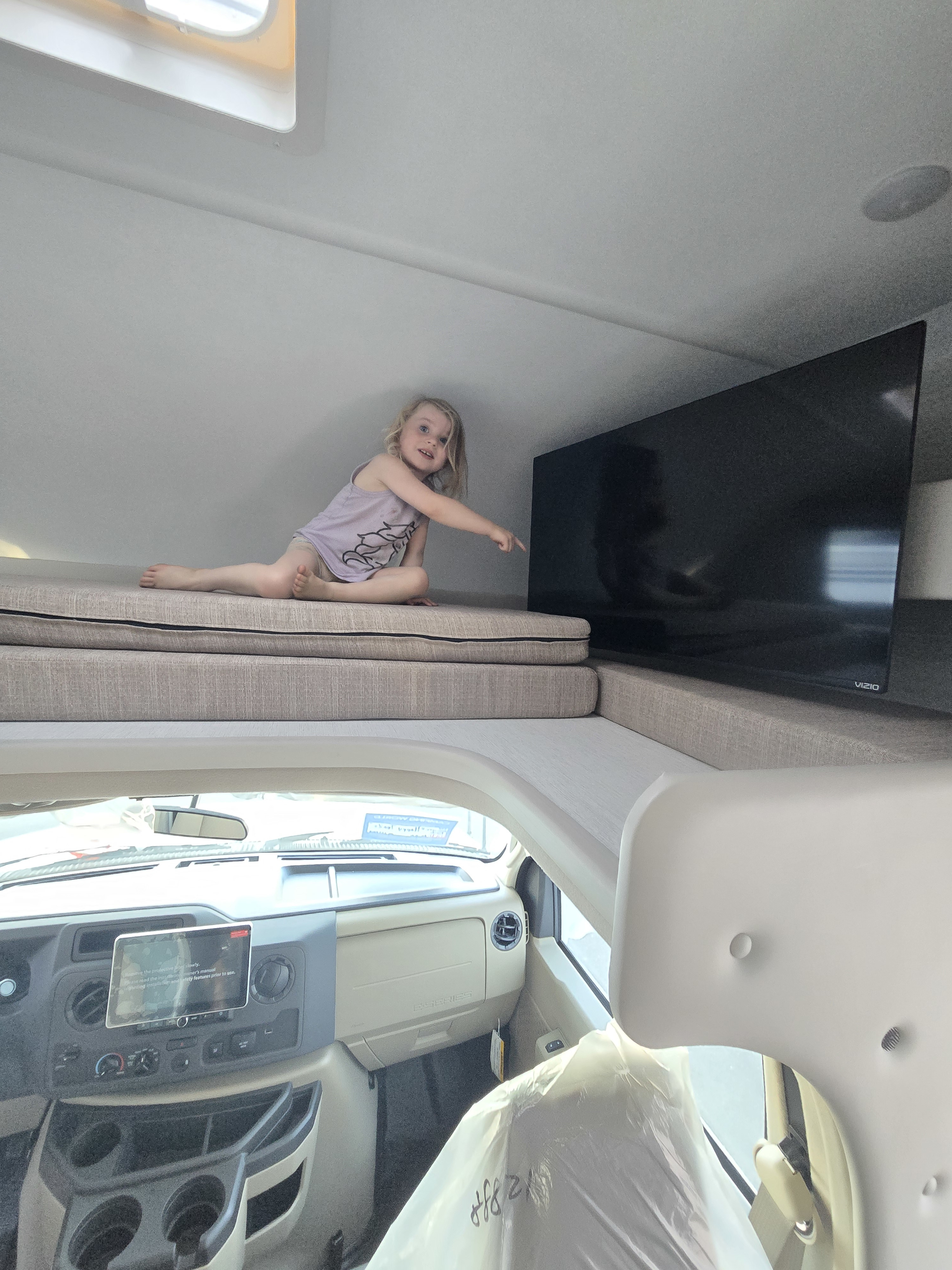 RV rental interior: A child points at a large TV mounted above the driver's cab bunk, ready for road trip entertainment.. Thor Eddie Bauer 22EB 2025