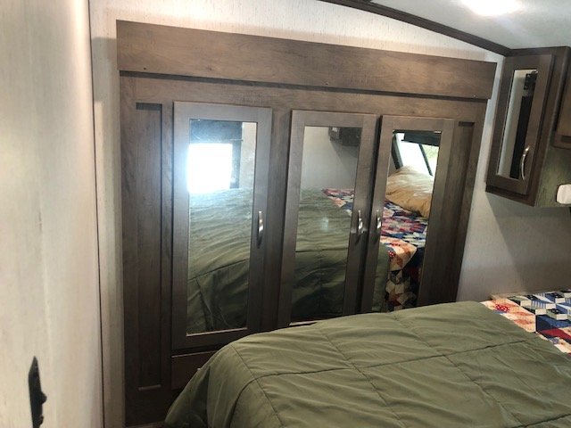 RV rental bedroom with a bed covered by a green comforter and quilt, alongside a three-door mirrored closet.. Astoria 1500 2021