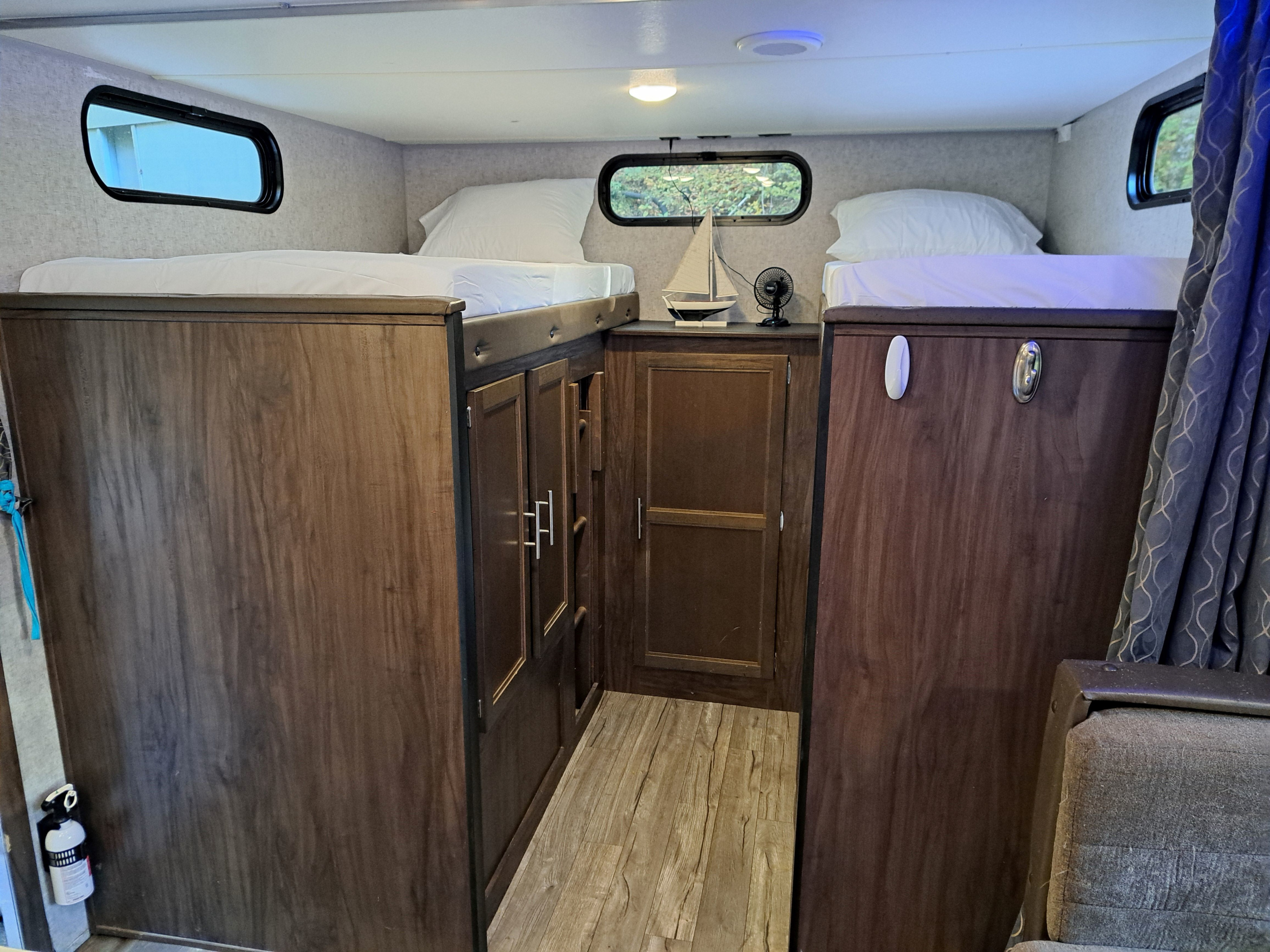 Inside an RV rental, featuring bunk beds with white linens, built-in storage, and small windows for a comfortable sleeping area.. Forest River Cherokee Grey Wolf 2019