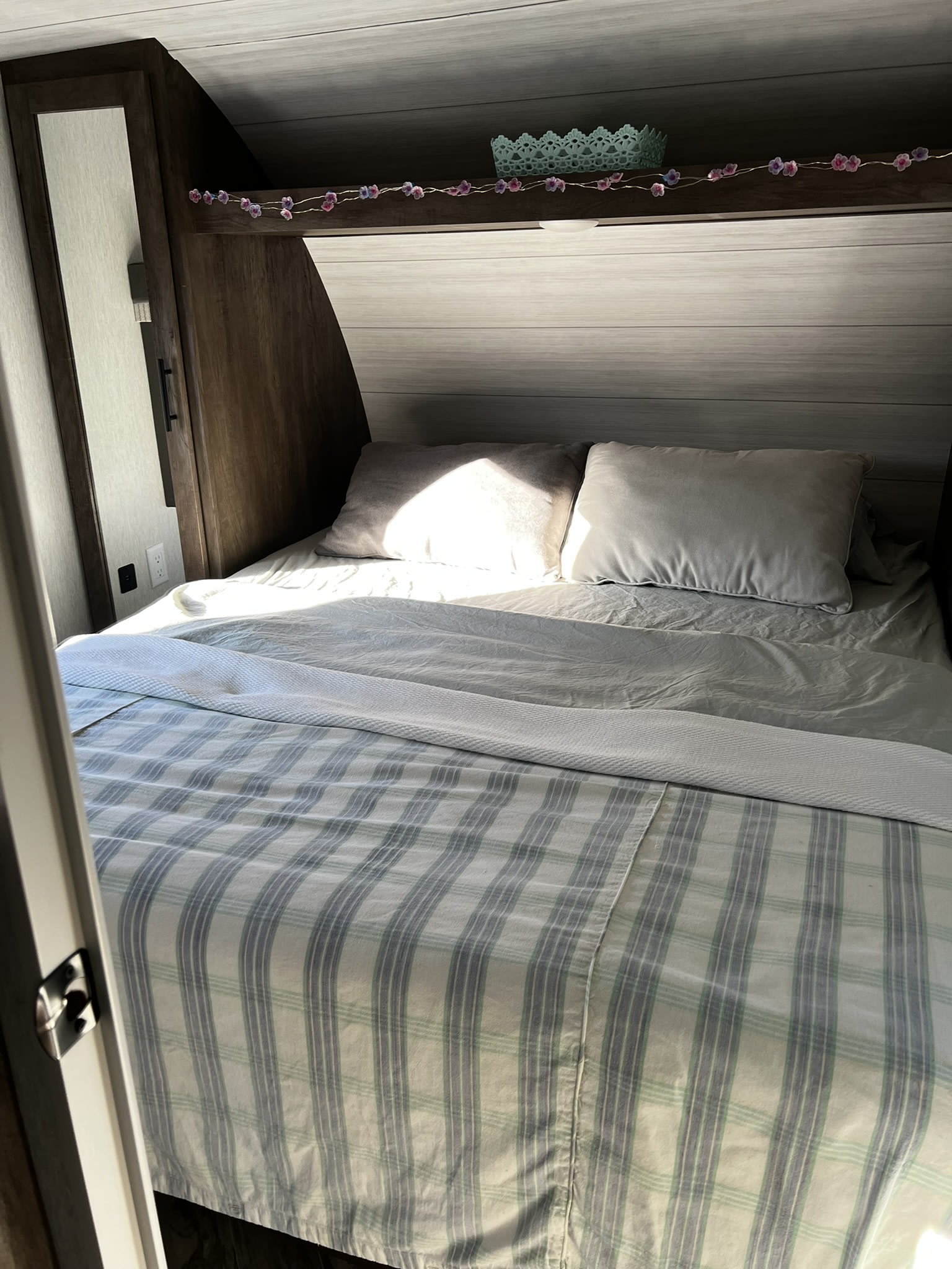 Cozy RV rental bedroom with a striped bedspread, soft pillows, and decorative flower lights above the bed.. Forest River Wildwood X-Lite 2022