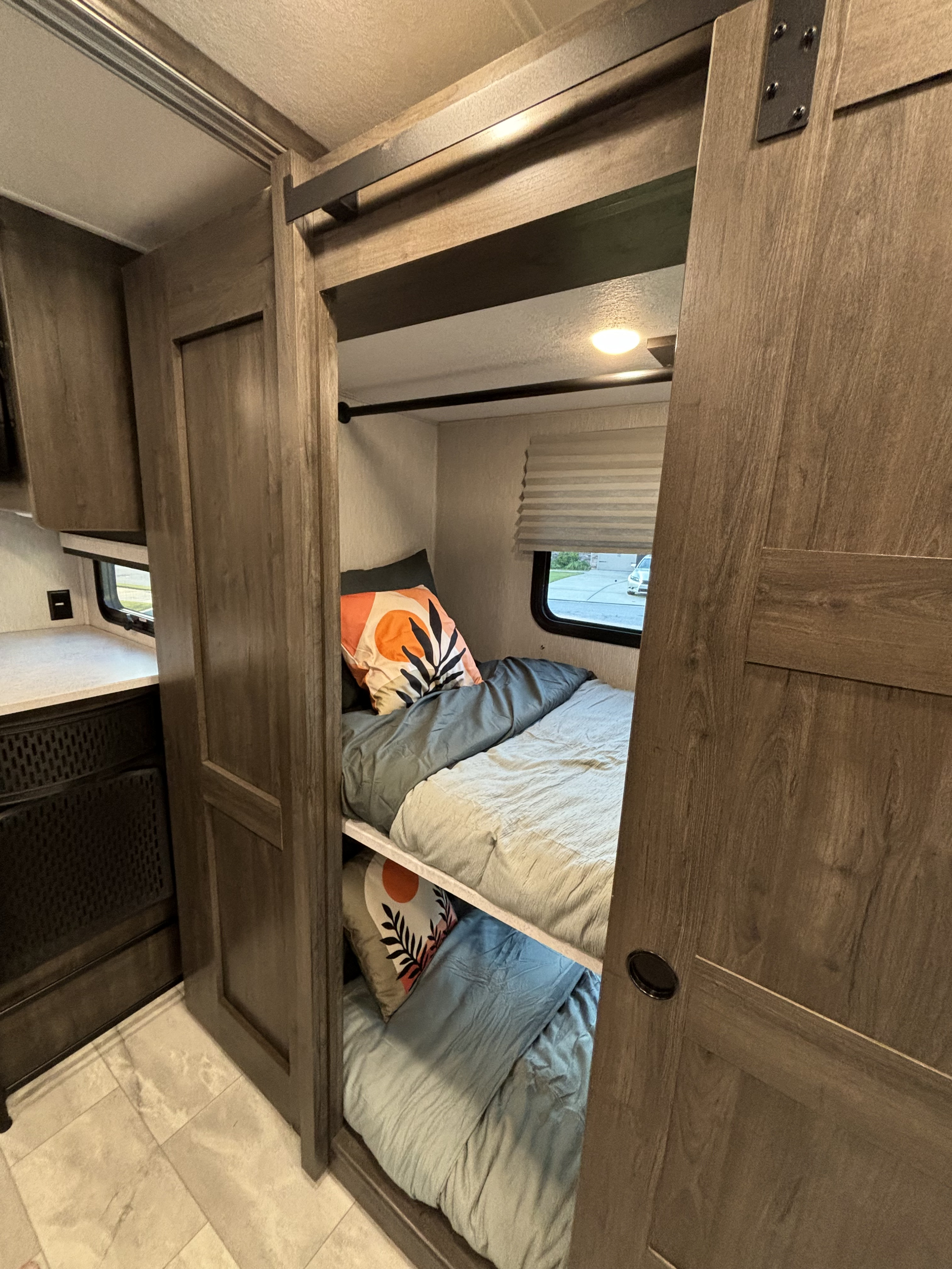 Cozy RV rental interior with comfortable bunk beds & stylish bedding, revealed by modern barn-style sliding doors.. Winnebago Coachmen 35ES Class A RV 2024