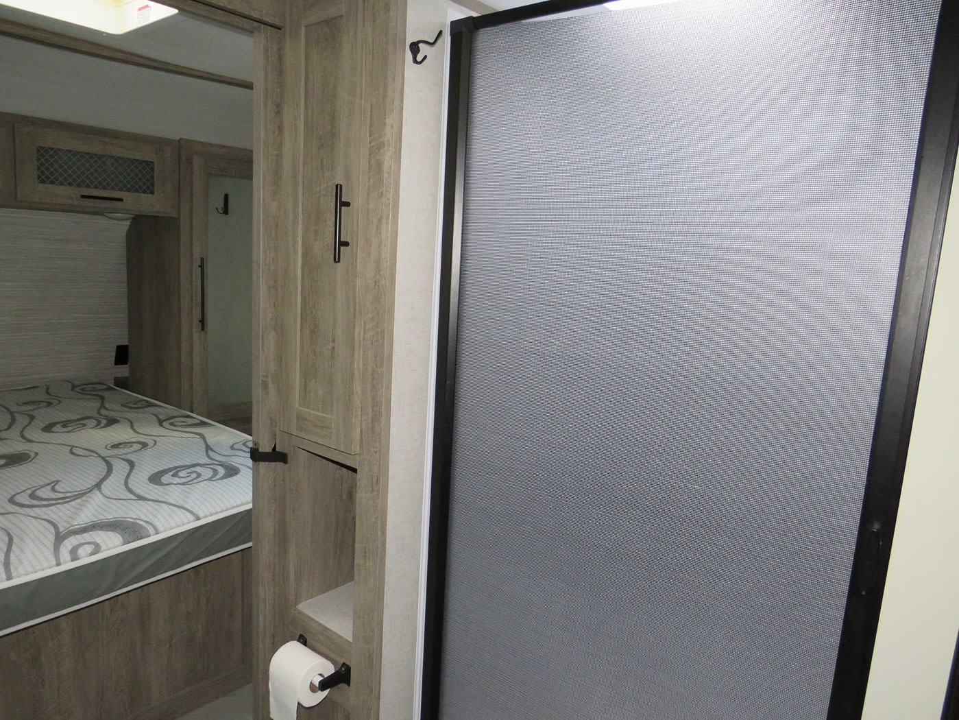 Compact RV rental interior with a bedroom, patterned mattress, wood cabinetry, and a shower door to a private bath.. Forest River Heritage Glen 2021
