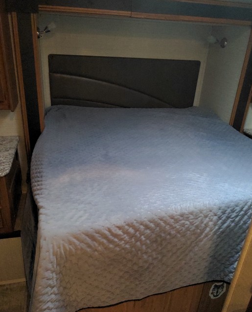 RV rental bedroom: a comfortable bed with a quilted cover, dark headboard, and wall-mounted reading lights.. Jayco Redhawk 2017