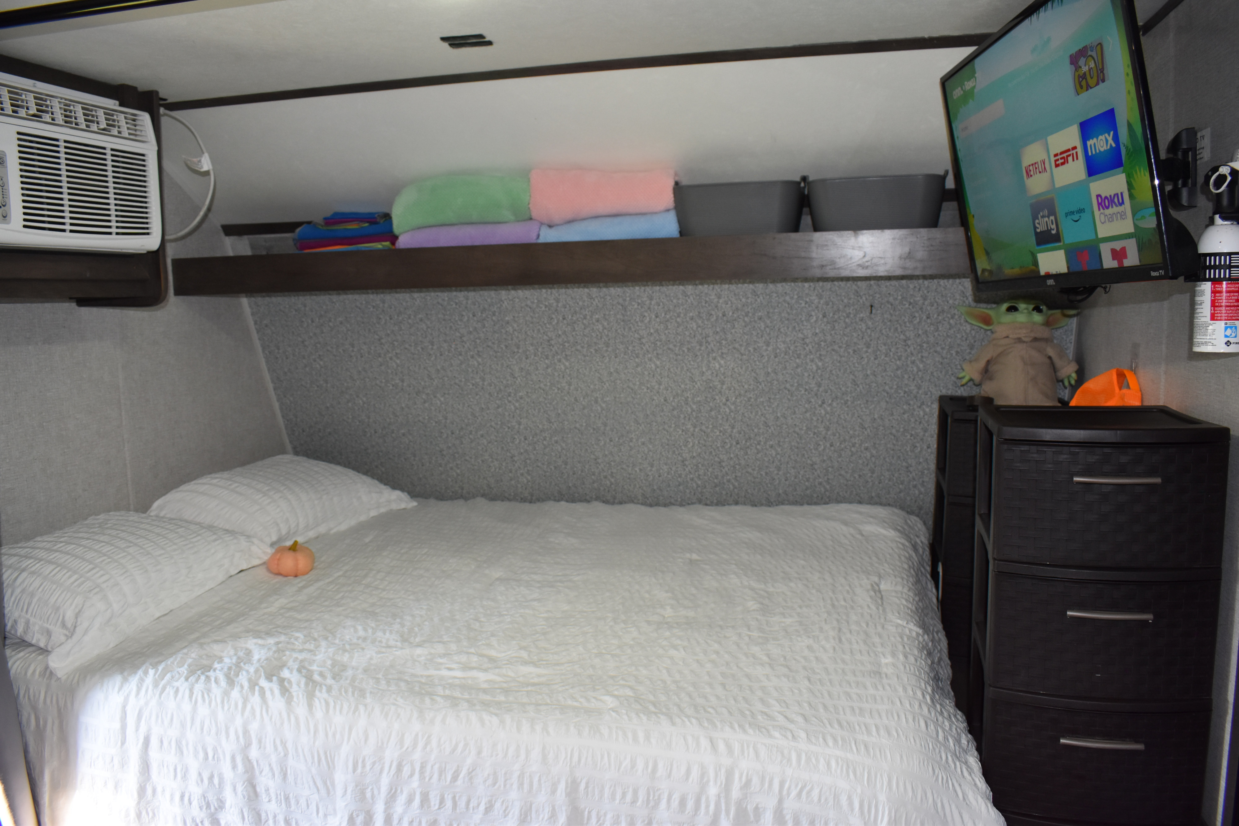 Comfortable RV rental bedroom with white bedding, overhead shelving, AC, TV, and bedside storage.. Dutchmen Coleman Lantern LT 2021