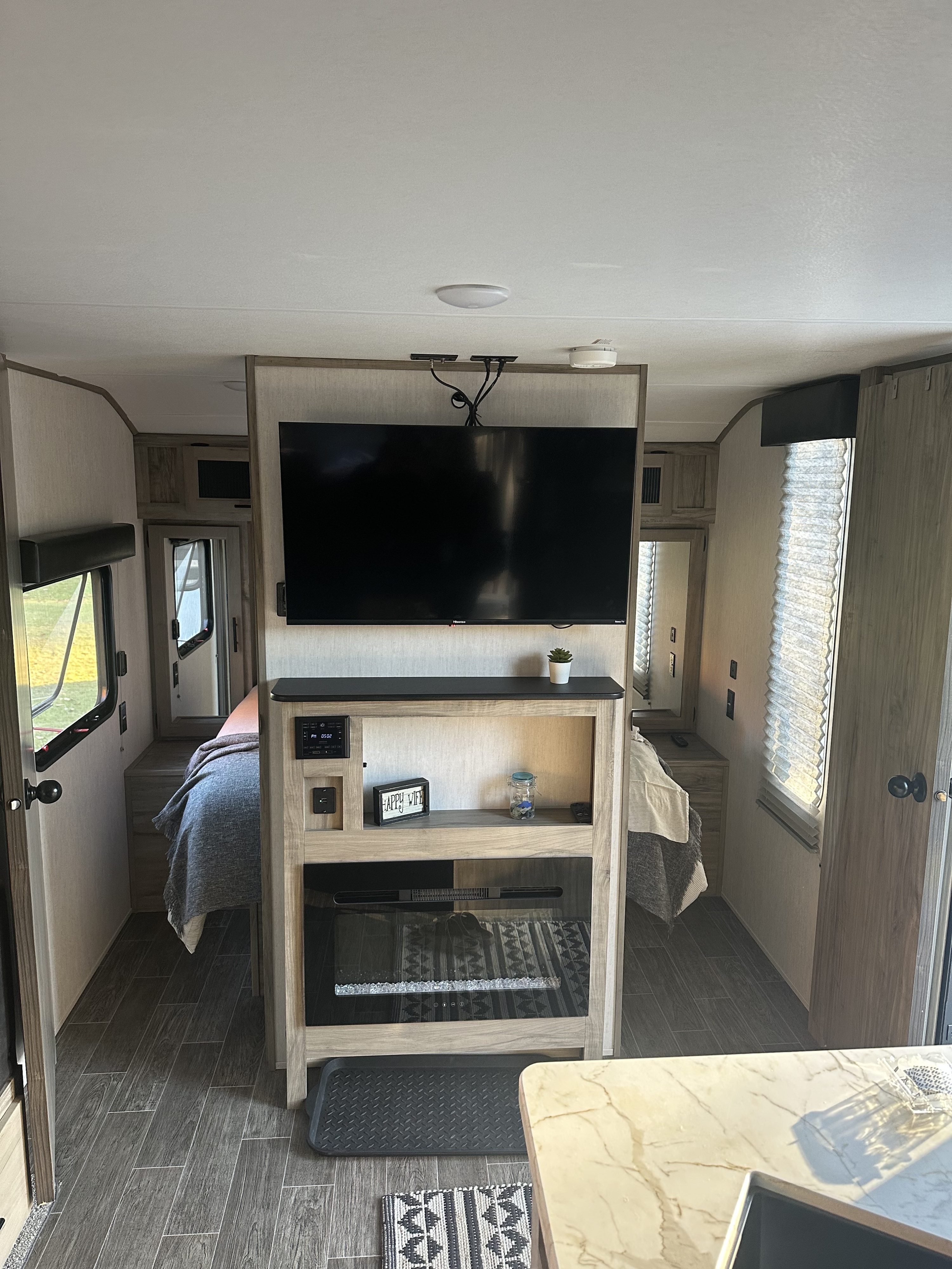 Inside a modern RV rental: view of the bedroom area, TV, and entertainment console with an electric fireplace.. Forest River Cherokee Alpha Wolf 2022