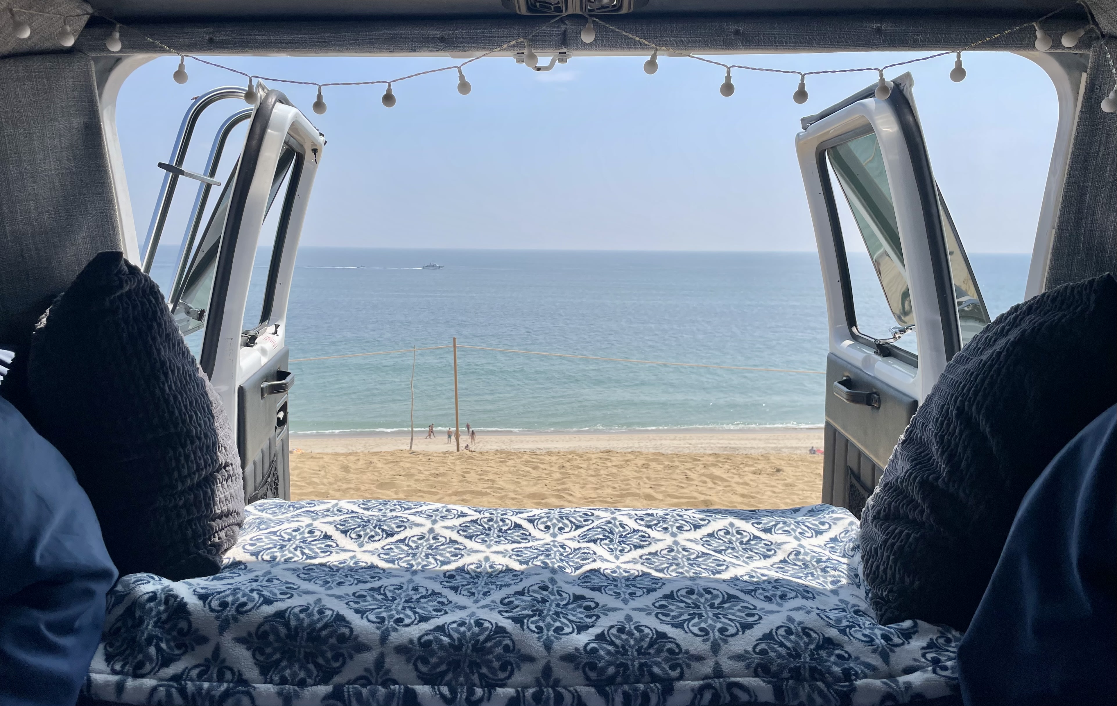 Relaxing **RV rental** view of a serene beach and ocean, with people and boats, from a cozy bed inside a camper van.. Roadtrek 210 - Popular 1996