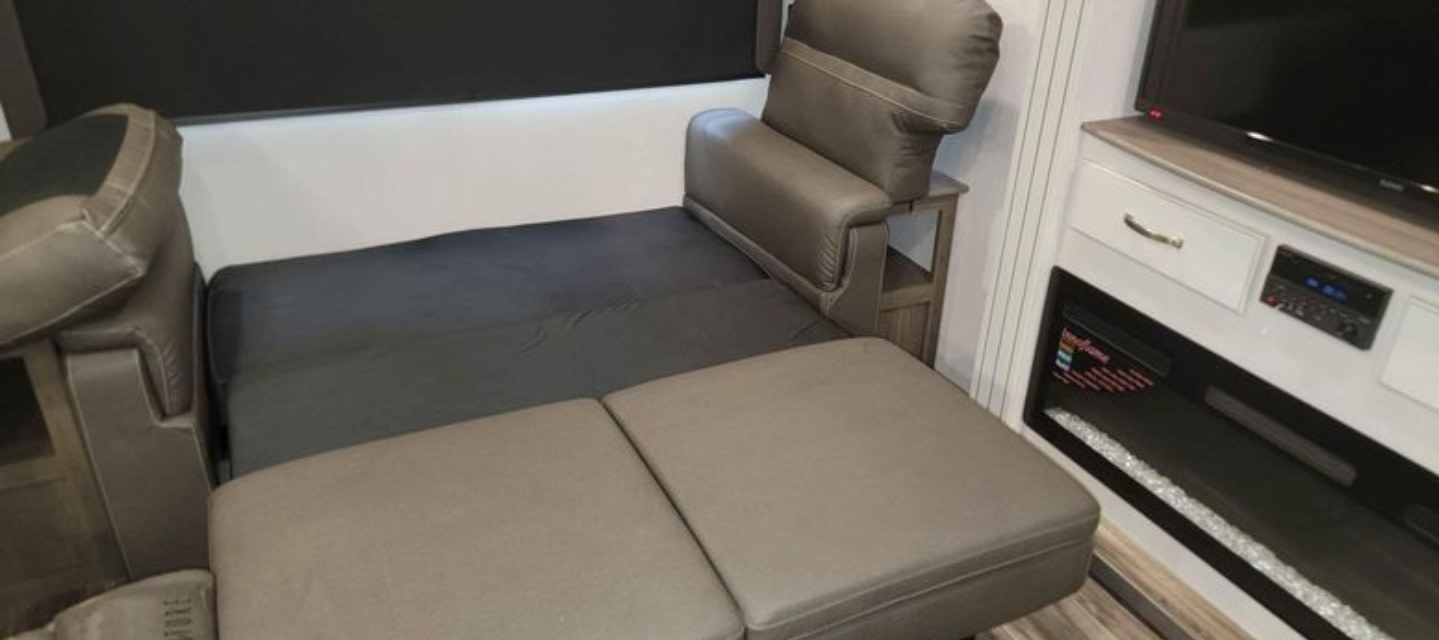 RV rental interior: A comfy convertible sofa bed next to an entertainment center with TV and electric fireplace.. Keystone RV Cougar 2023