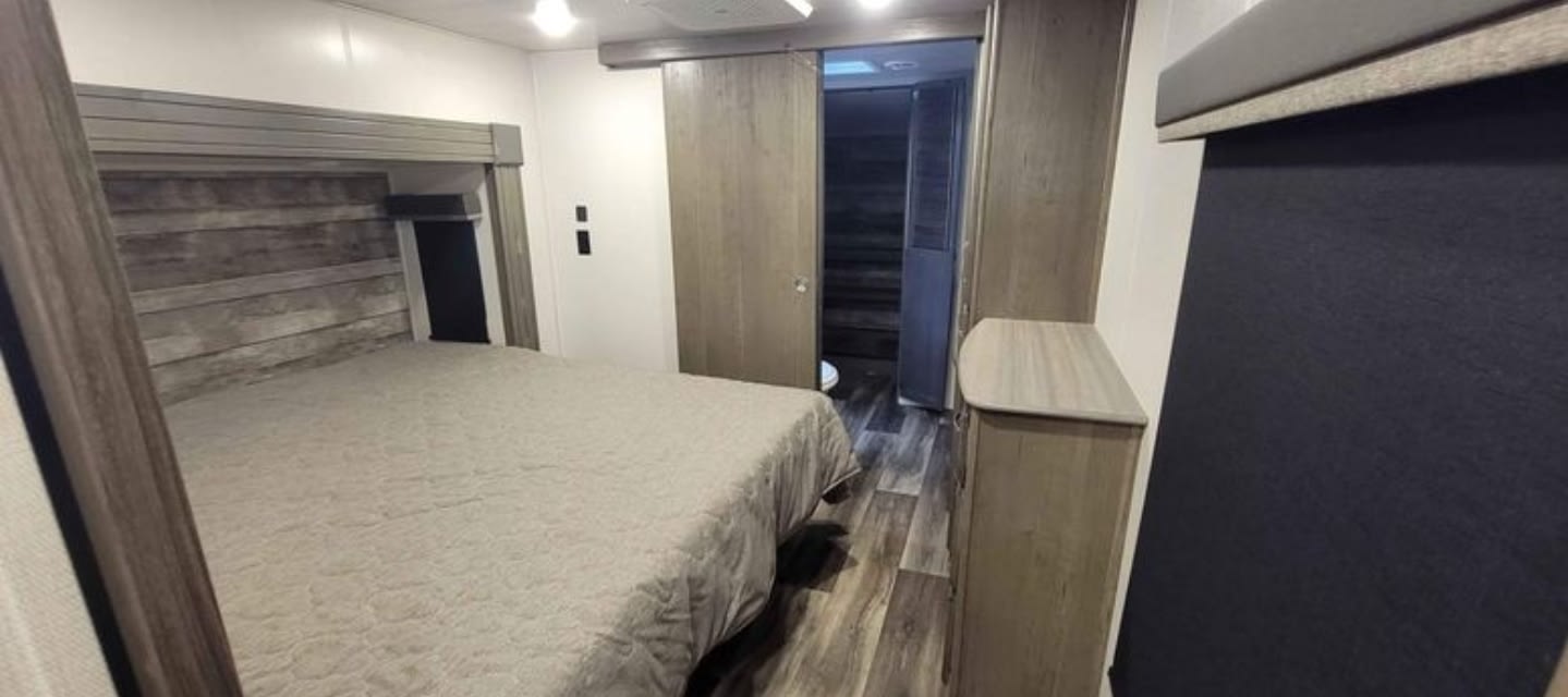 Comfortable RV rental bedroom features a queen bed, wooden accents, and private sliding doors.. Keystone RV Cougar 2023