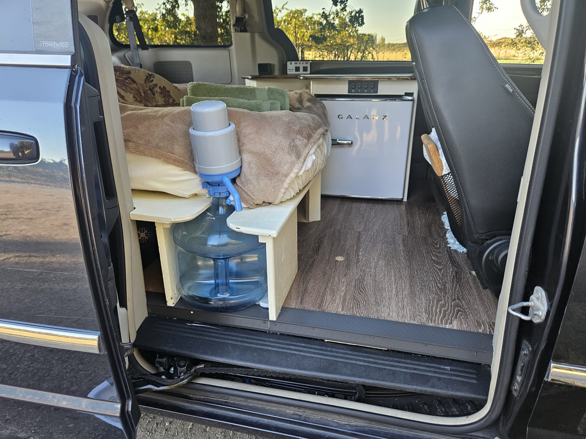 Inside an RV rental: a custom bed with water, a retro mini-fridge, and wood floors for van life adventures.. Chrysler Town Country 2013
