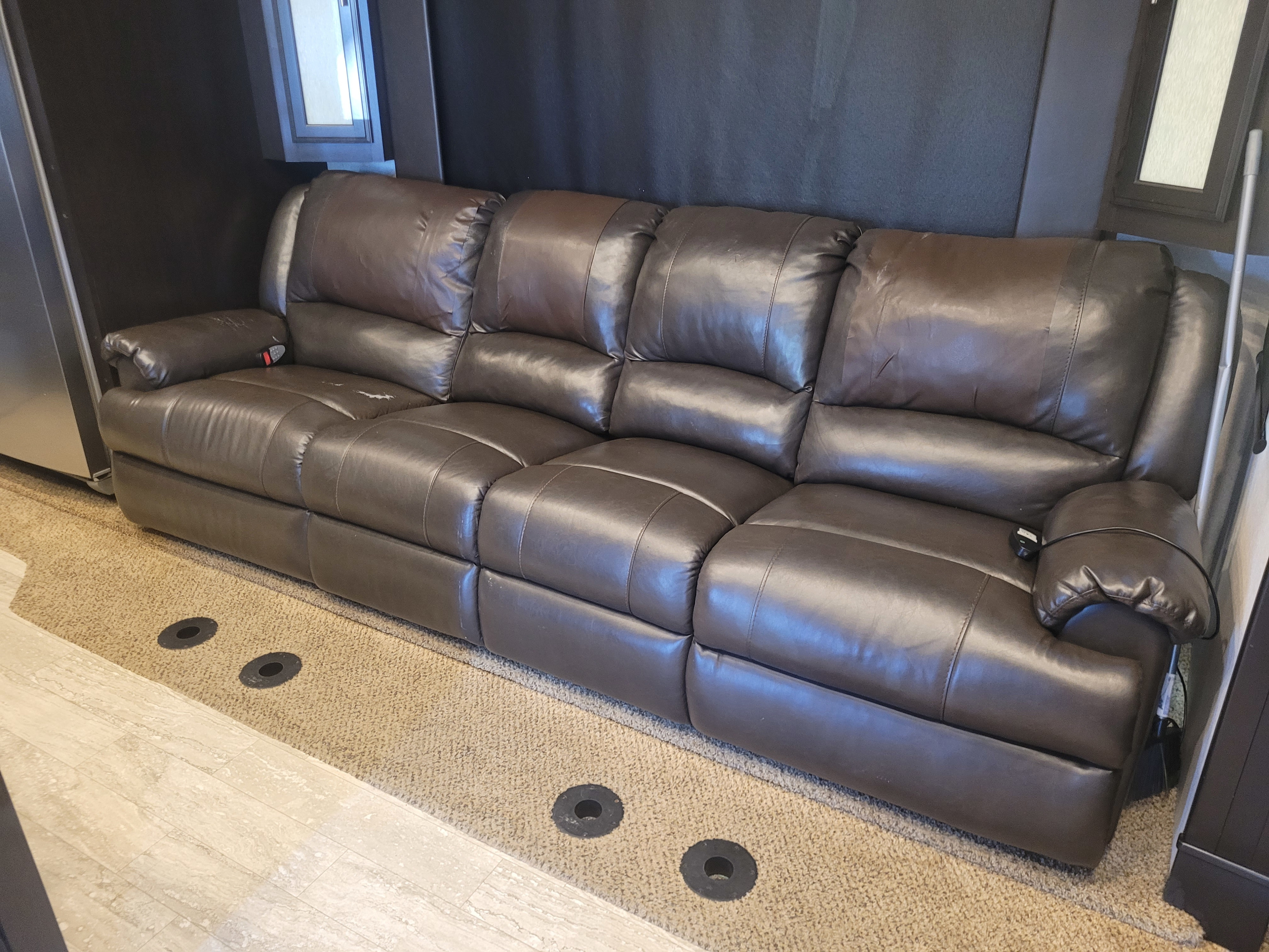 A plush brown leather reclining sofa is featured in an RV rental interior, offering comfortable seating with visible floor anchors.. Jayco Seismic 2017