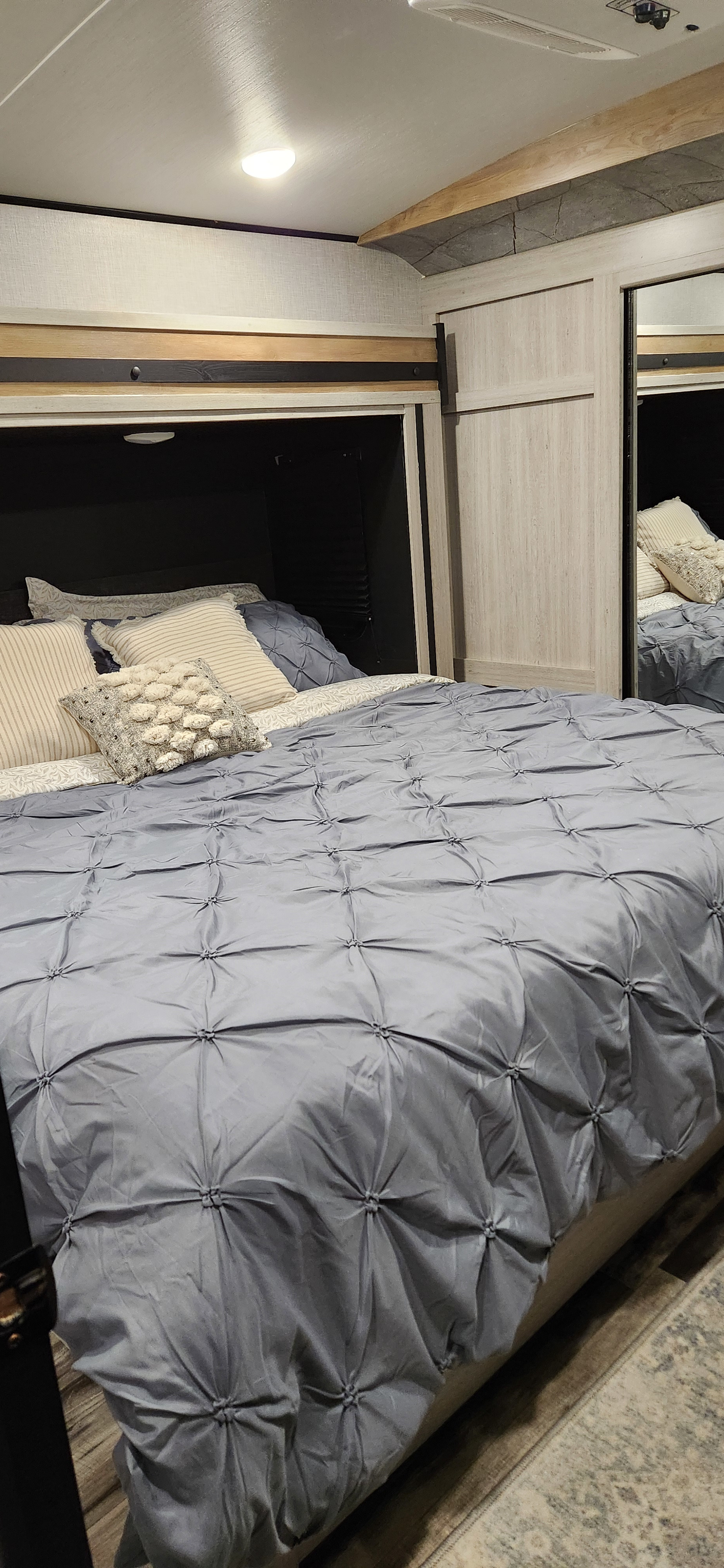 Cozy RV rental bedroom featuring a grey comforter, assorted pillows, and built-in storage with overhead lighting.. Crossroads RV SS330SI 2024