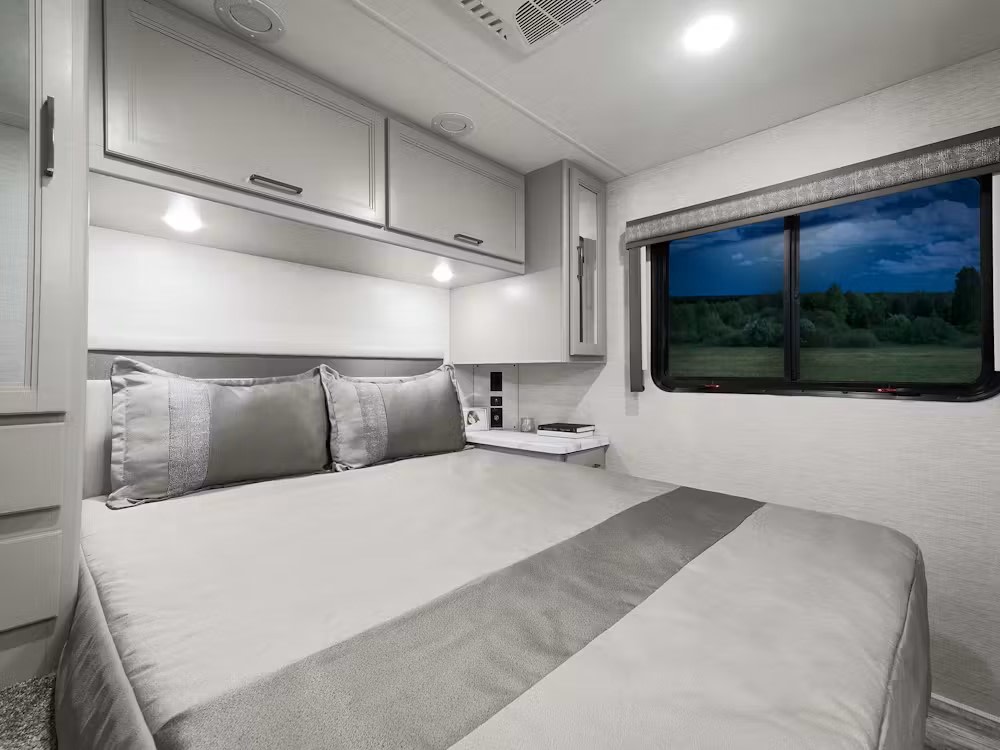 Comfortable RV rental bedroom with modern decor, a cozy bed, and a scenic nature view from the window.. Thor Chateau 2024