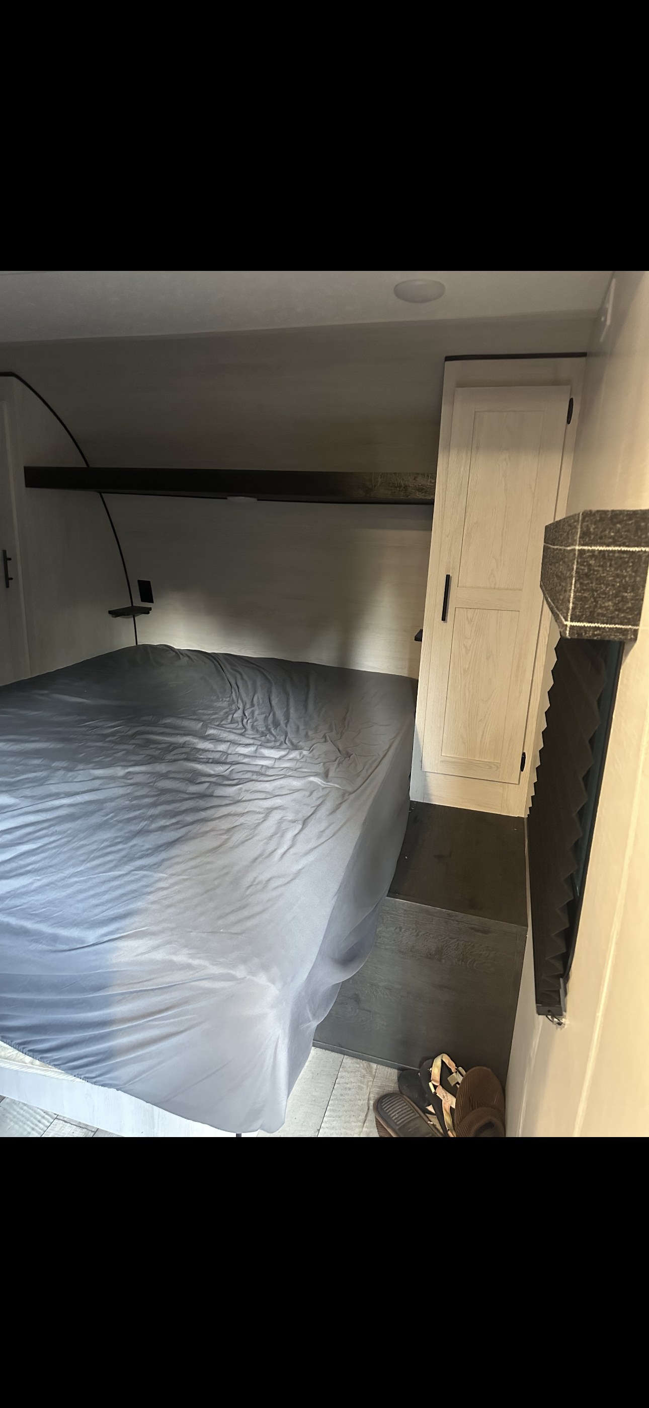 Inside an RV rental, a compact bedroom features a grey bed, light wood wardrobe, and dark flooring. Ideal for travelers.. Sportsmen SE 2023