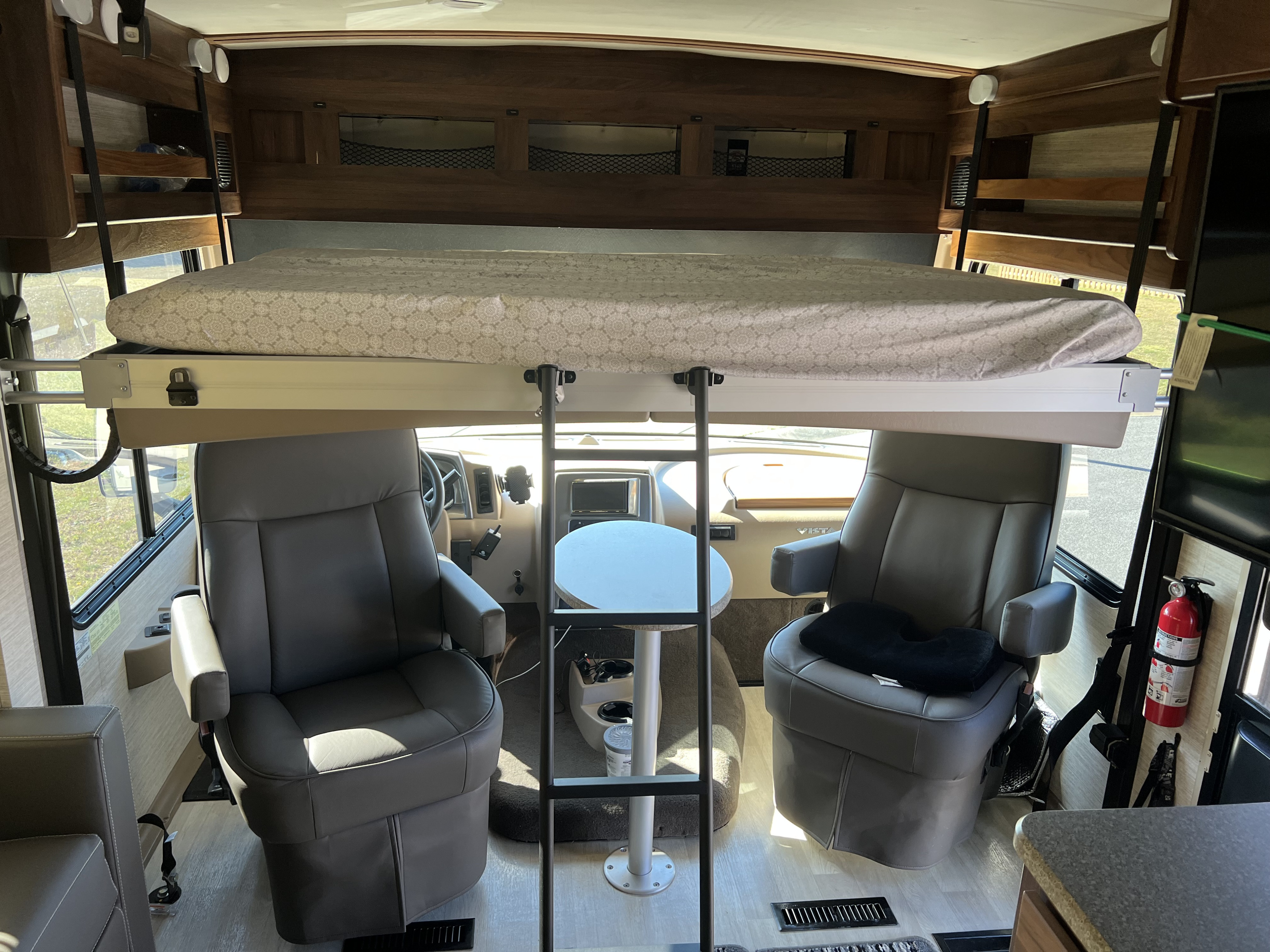 RV rental interior with a drop-down bunk bed above the cockpit, swivel seats, and a small table.. Winnebago Vista 2021