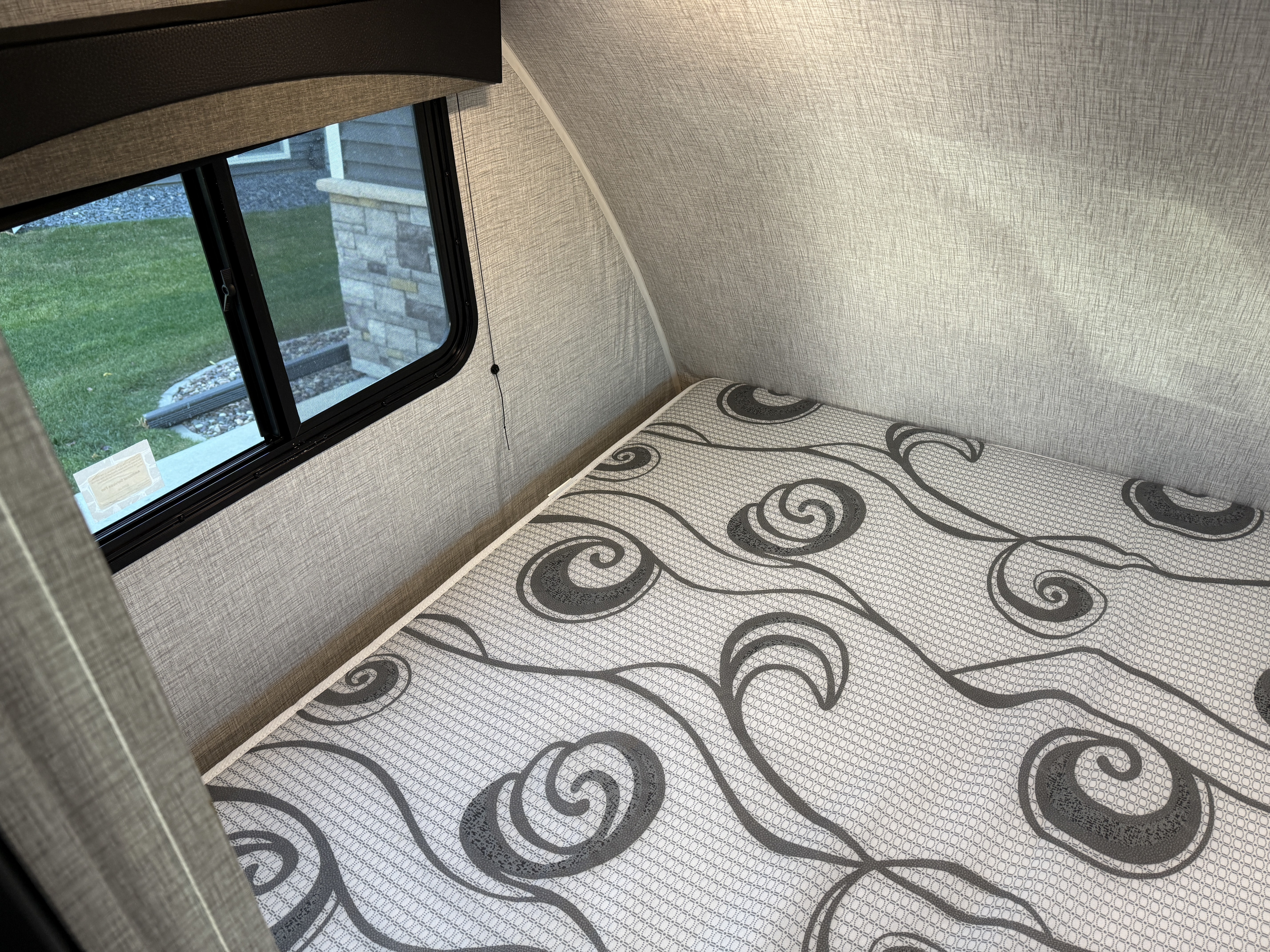 RV rental interior: a clean, compact bedroom with a unique patterned mattress and window showcasing outdoor views.. Braxton Creek Bushwhacker Plus 2022