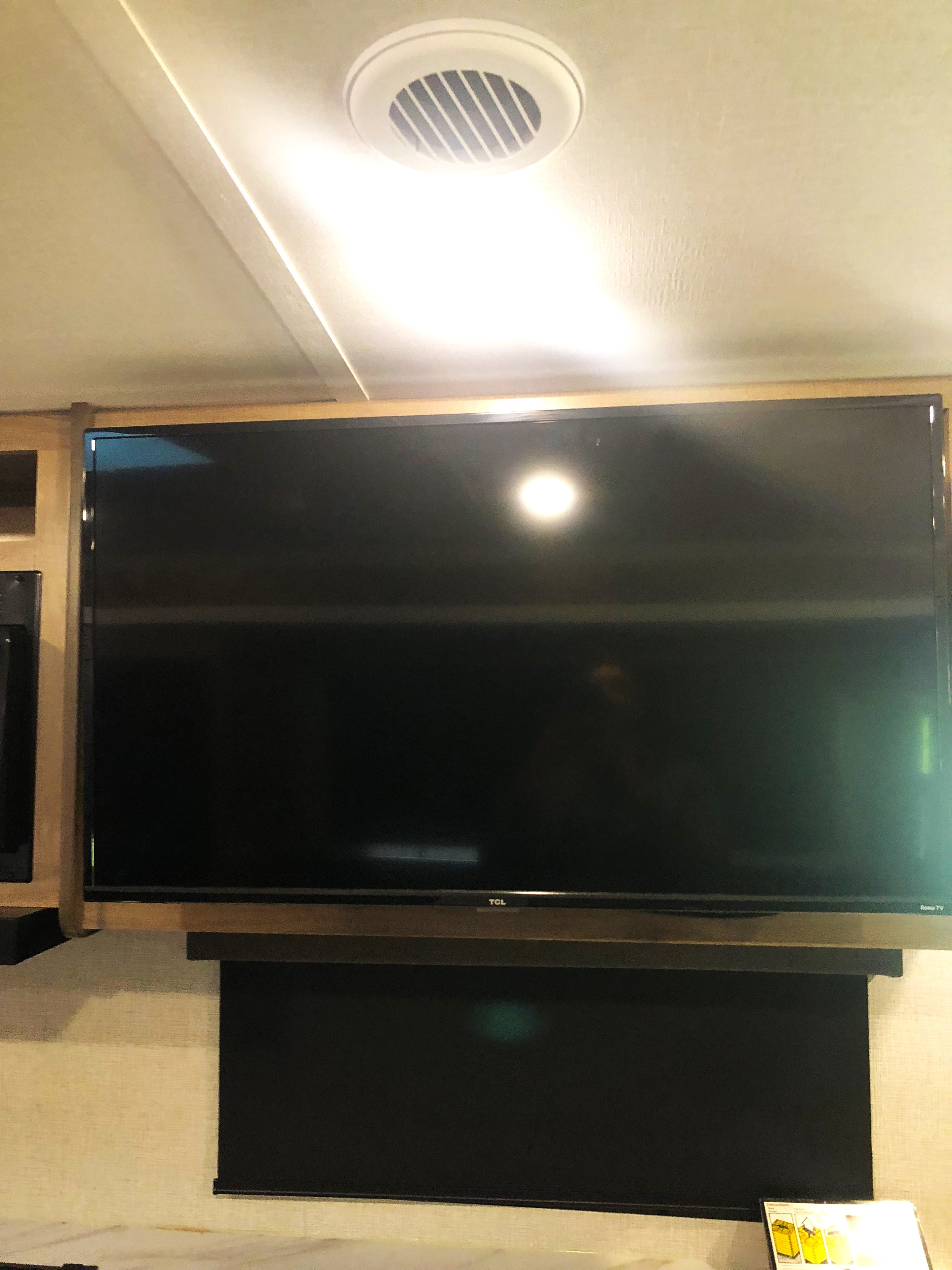 This RV rental's interior features a mounted flat-screen TV under a ceiling vent, with a dark roller blind below.. Grand Design Imagine 2023