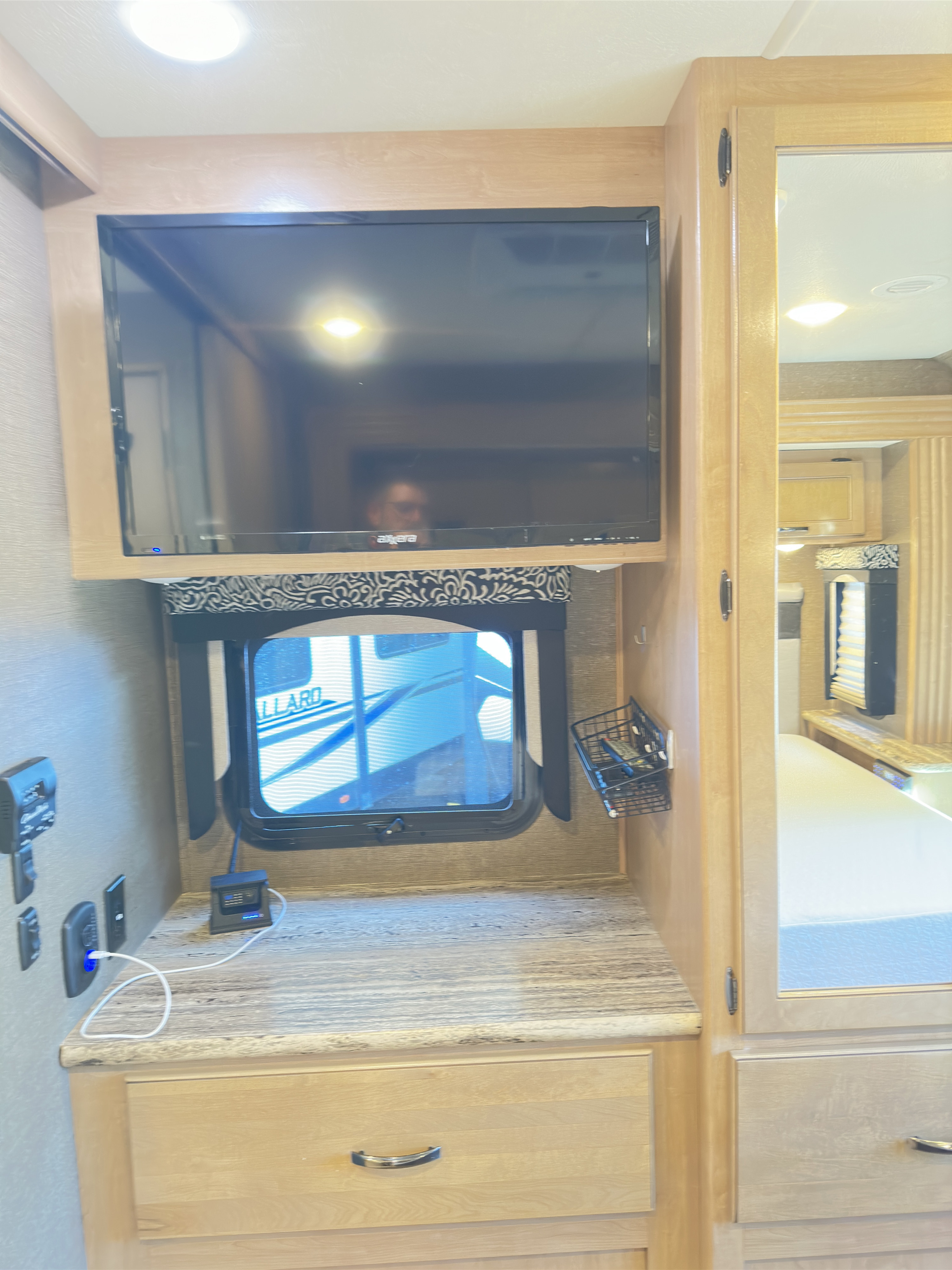 Inside an RV rental: a cozy bedroom area with wall-mounted TV, countertop, charging station, and mirrored closet.. Thor A.C.E. 2018