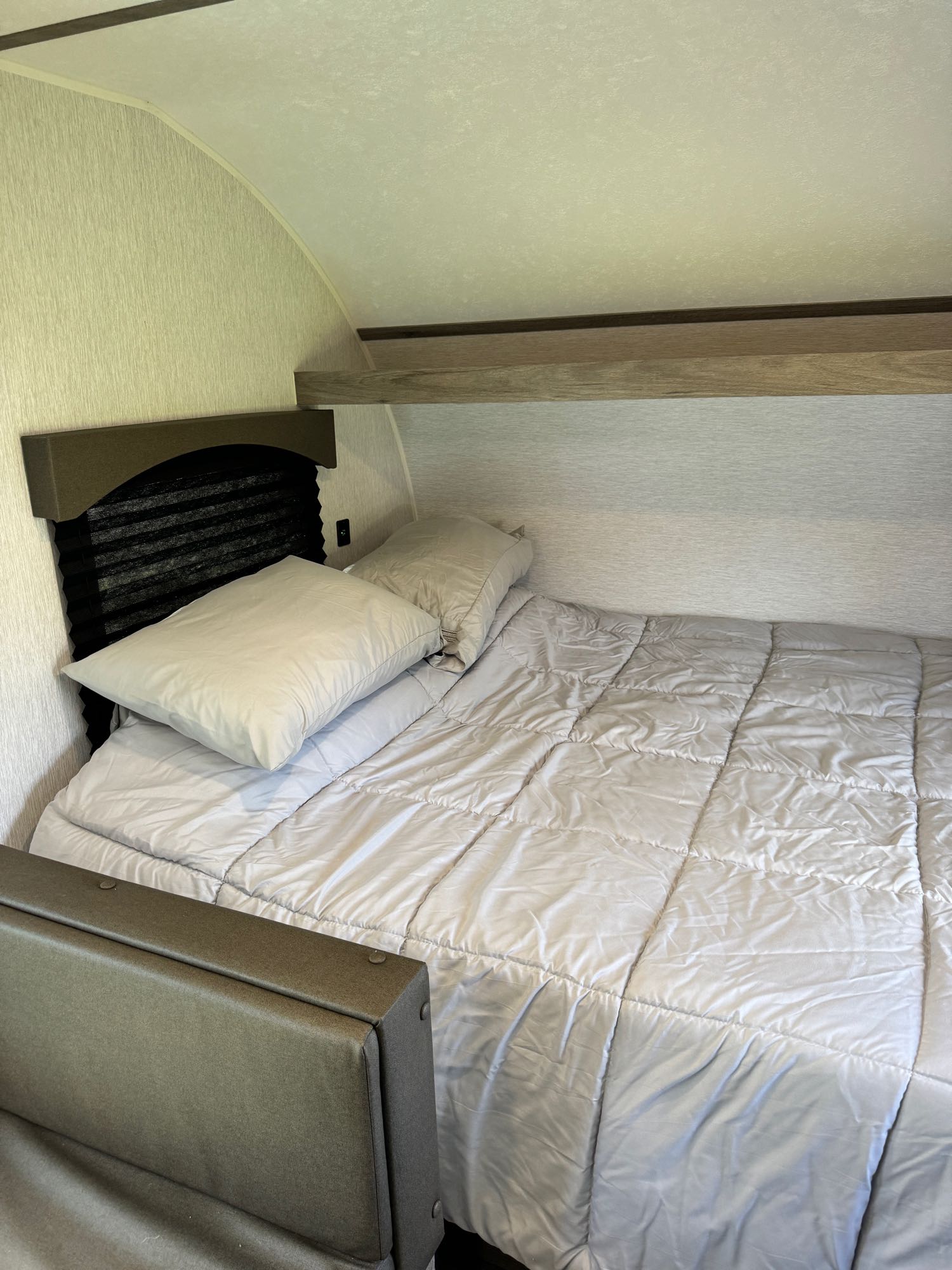 This RV rental features a cozy bed with soft bedding, pillows, and a practical overhead shelf for comfortable travel.. Sunset Park RV Sun Lite LTD 2024