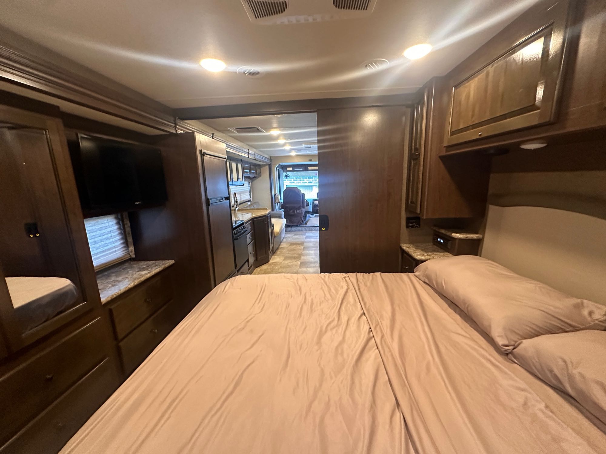 Cozy RV rental interior: Bedroom with light bed and TV, opens to a full kitchen and front living area.. Thor Windsport 2018