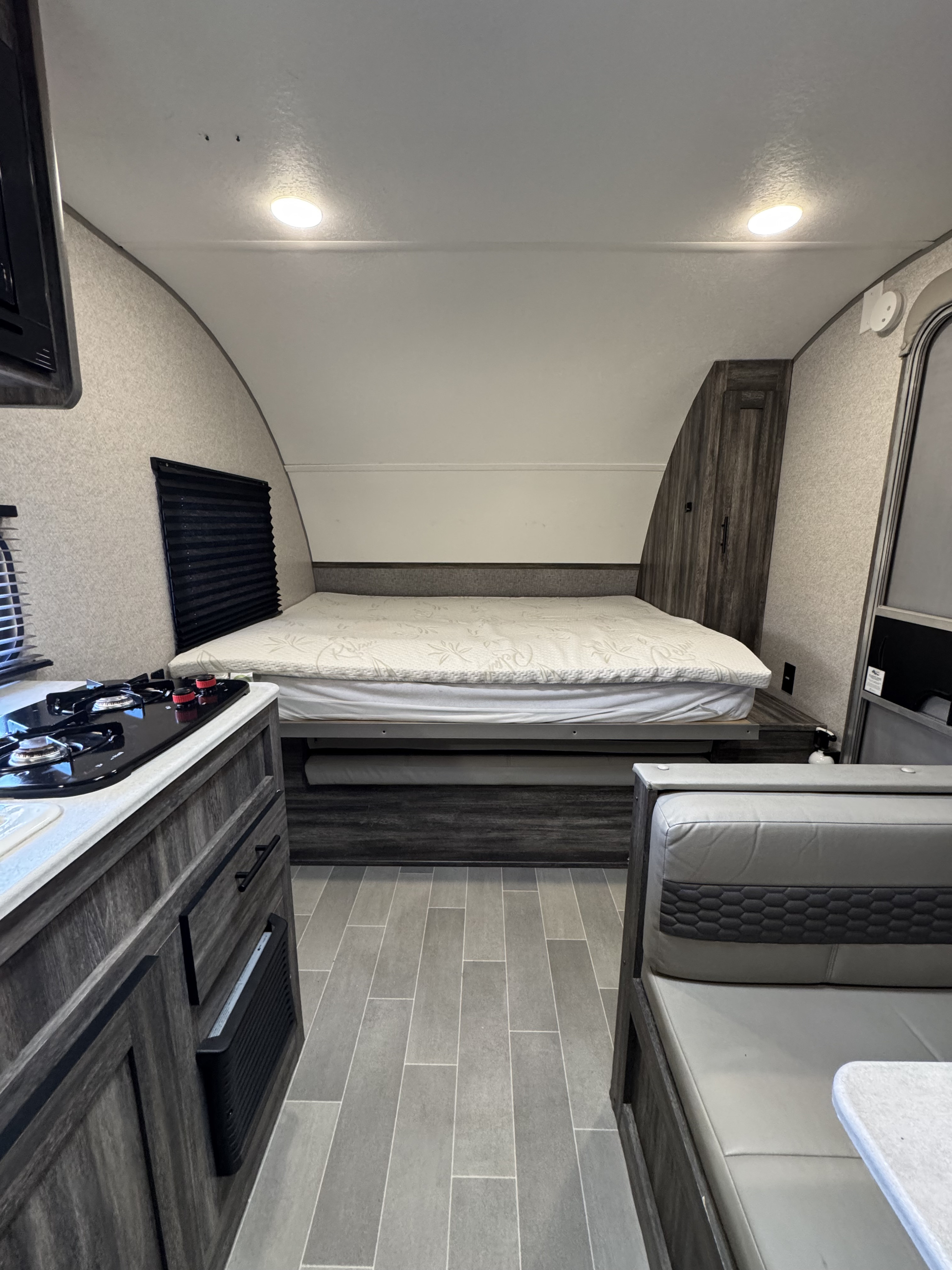 View of a modern RV rental interior showing a large bed, a two-burner stove on a counter, and dinette seating.. Forest River Salem FSX 2020