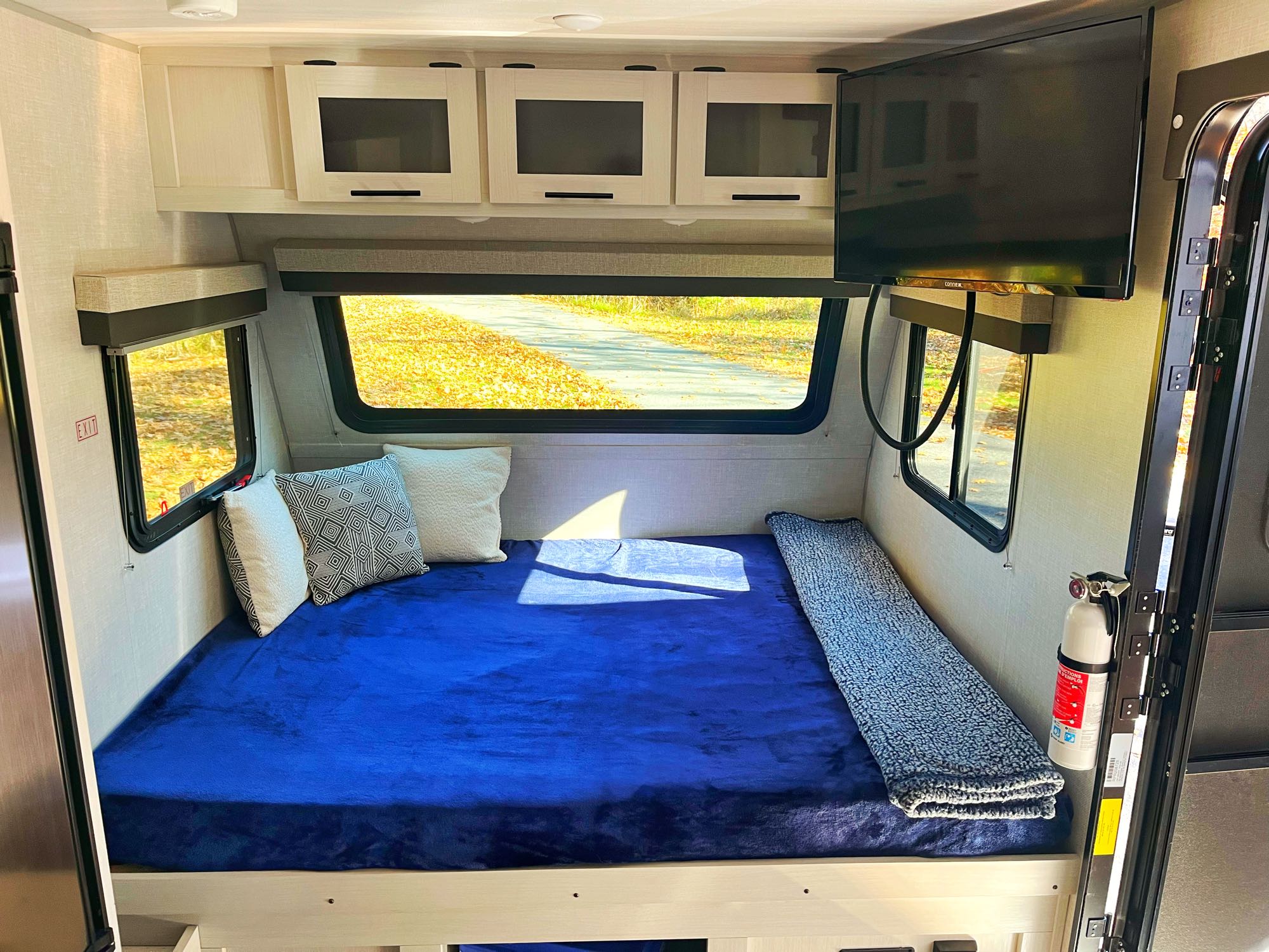 Comfortable RV rental sleeping area with a vibrant blue bed, windows showcasing nature, and convenient overhead storage.. No Boundaries 16.6 2023