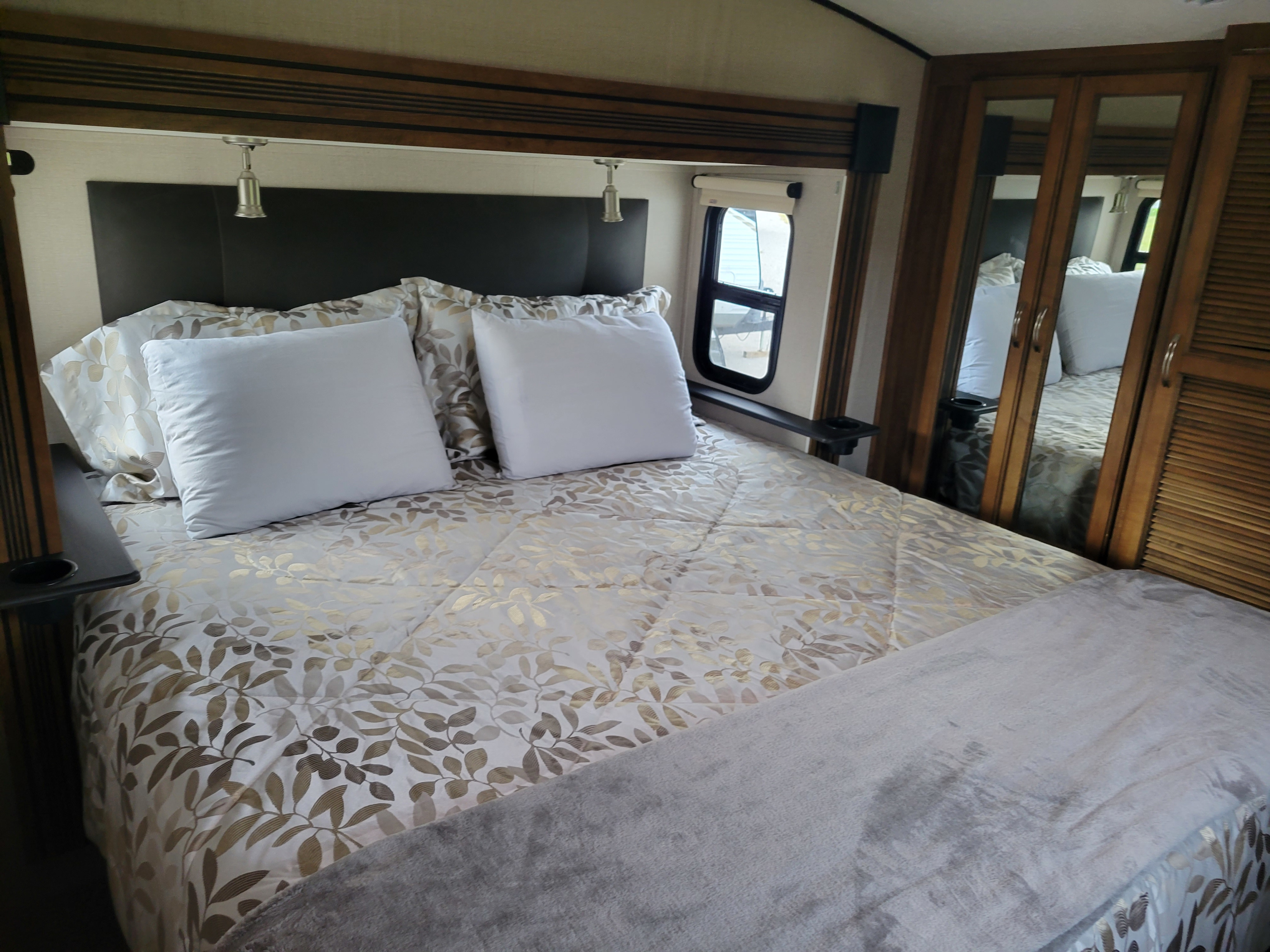 Comfortable RV rental bedroom featuring patterned bedding, white pillows, reading lights, and a mirrored closet door.. Forest River Chaparral 2018