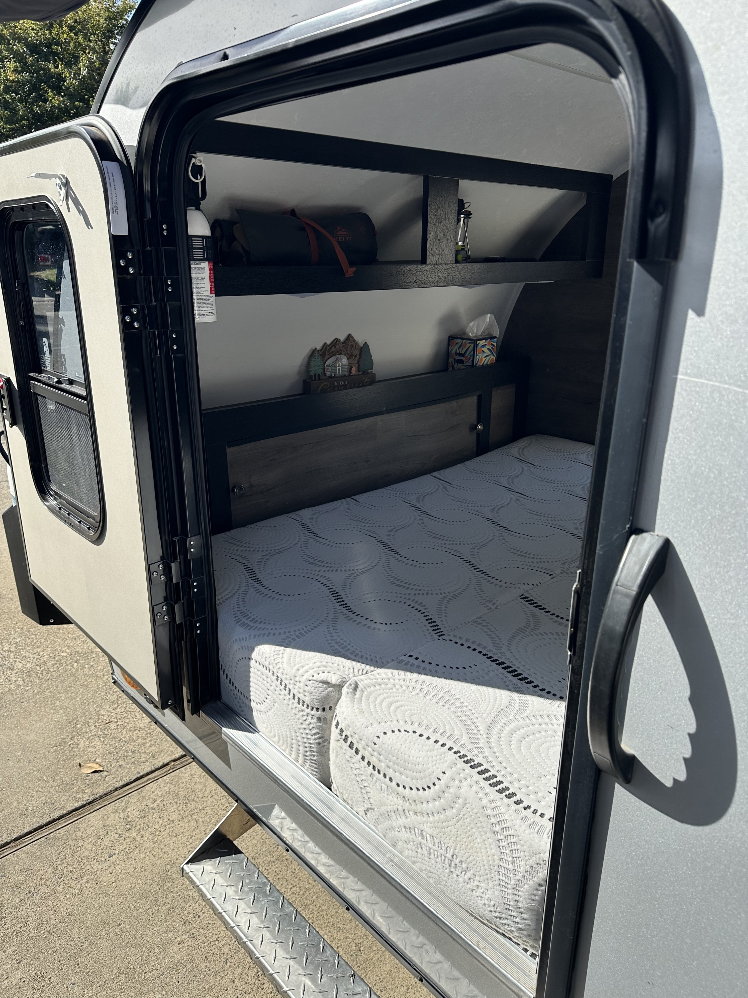 Inside a cozy rv rental: patterned mattress, dark wood headboard with cubbies, and shelves for camping essentials.. Braxton Creek Bushwhacker 2021