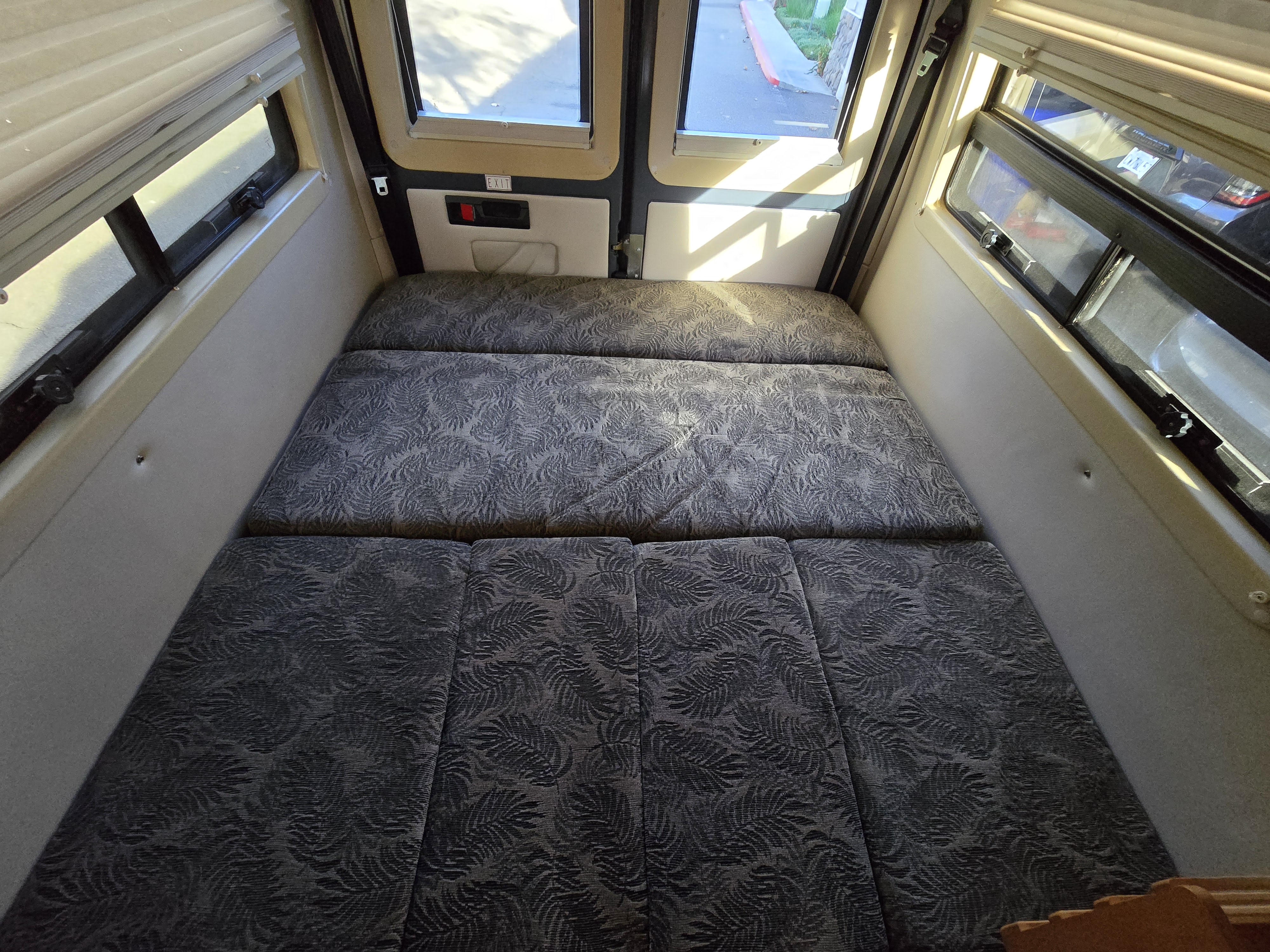 Overhead view of an RV rental's rear bed/seating area with patterned cushions and windows, ideal for travel.. Leisure Travel Vans Leisure Travel Vans Class B 2004