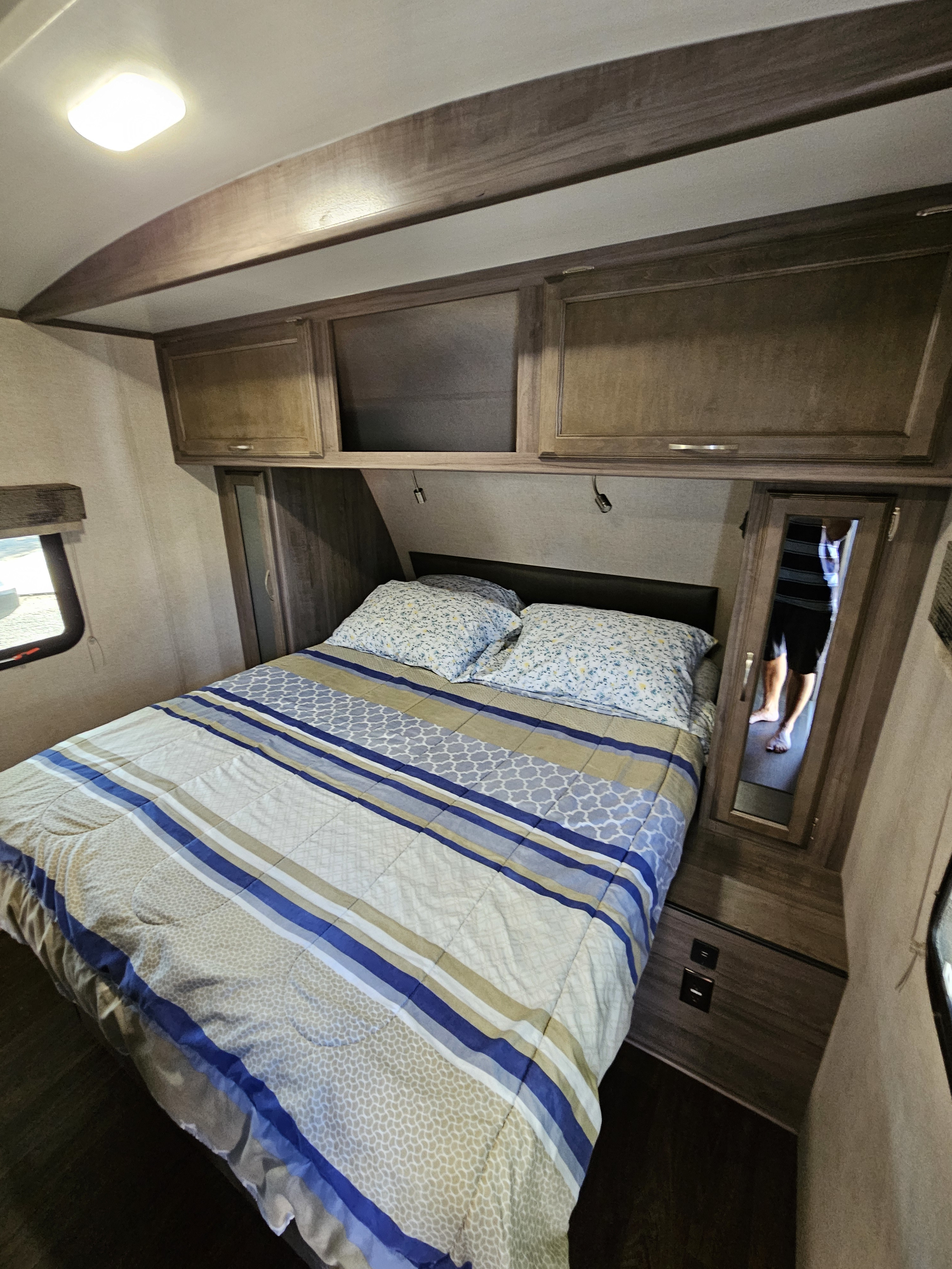 Cozy RV rental bedroom with patterned bedding, overhead storage, and mirror. Features include a comfortable bed and charging ports.. Minnie Minnie Plus 2019