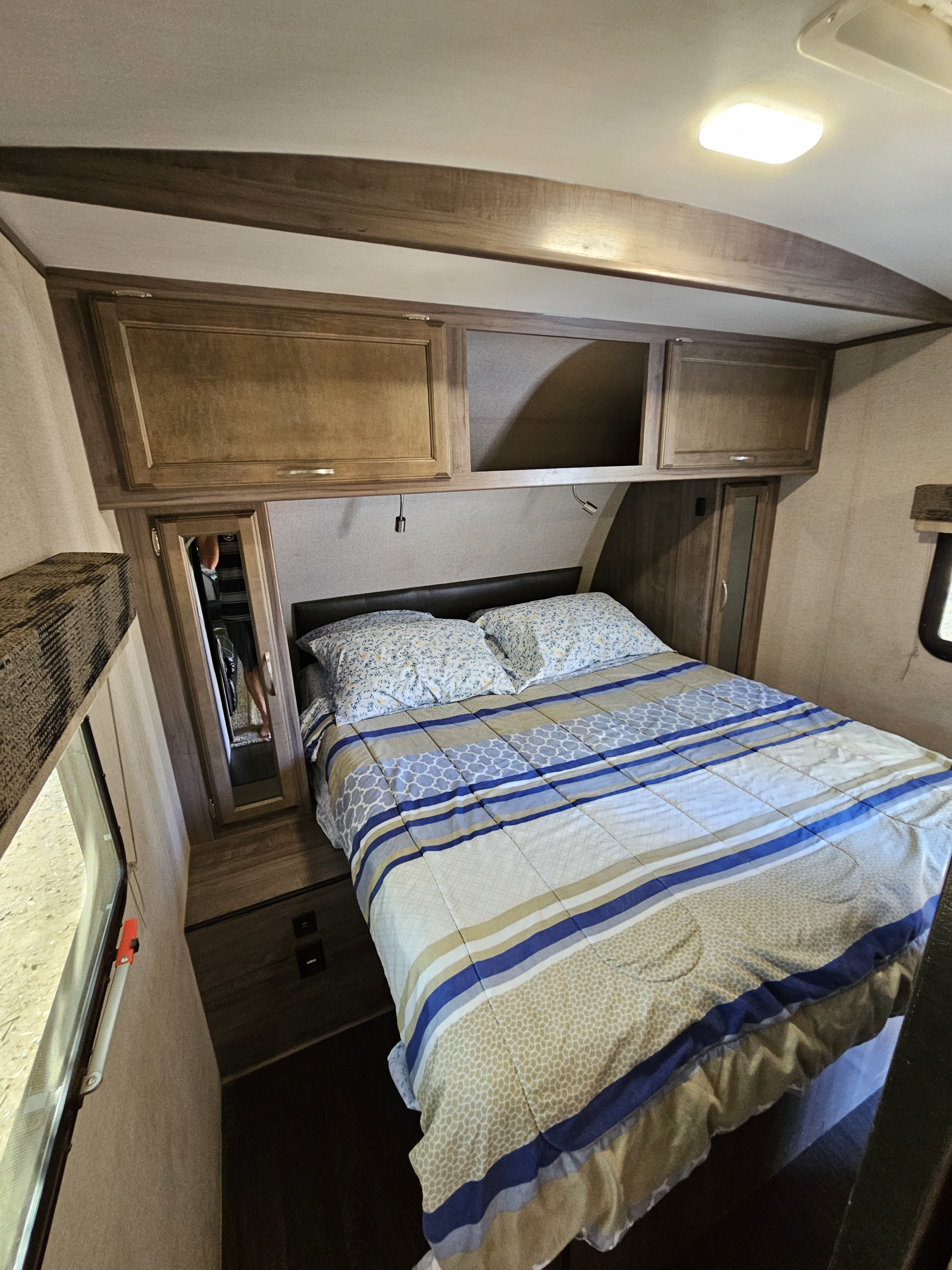 Cozy RV rental bedroom featuring a full-size bed with patterned bedding, wood cabinets, and a reflective closet.. Minnie Minnie Plus 2019
