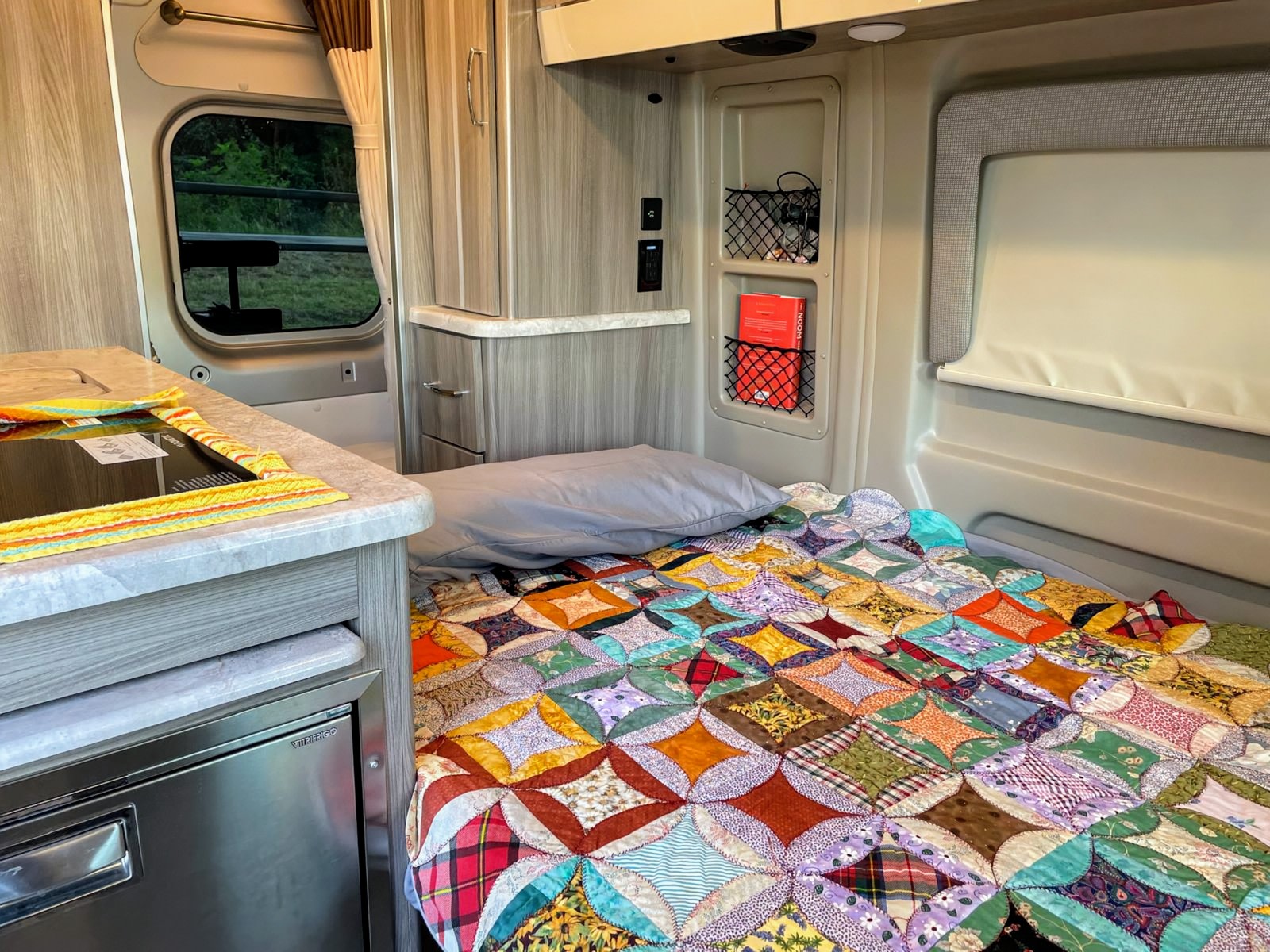 Cozy RV rental interior with a colorful bed, compact kitchen, and scenic window view, ready for adventure.. Thor Scope 2024