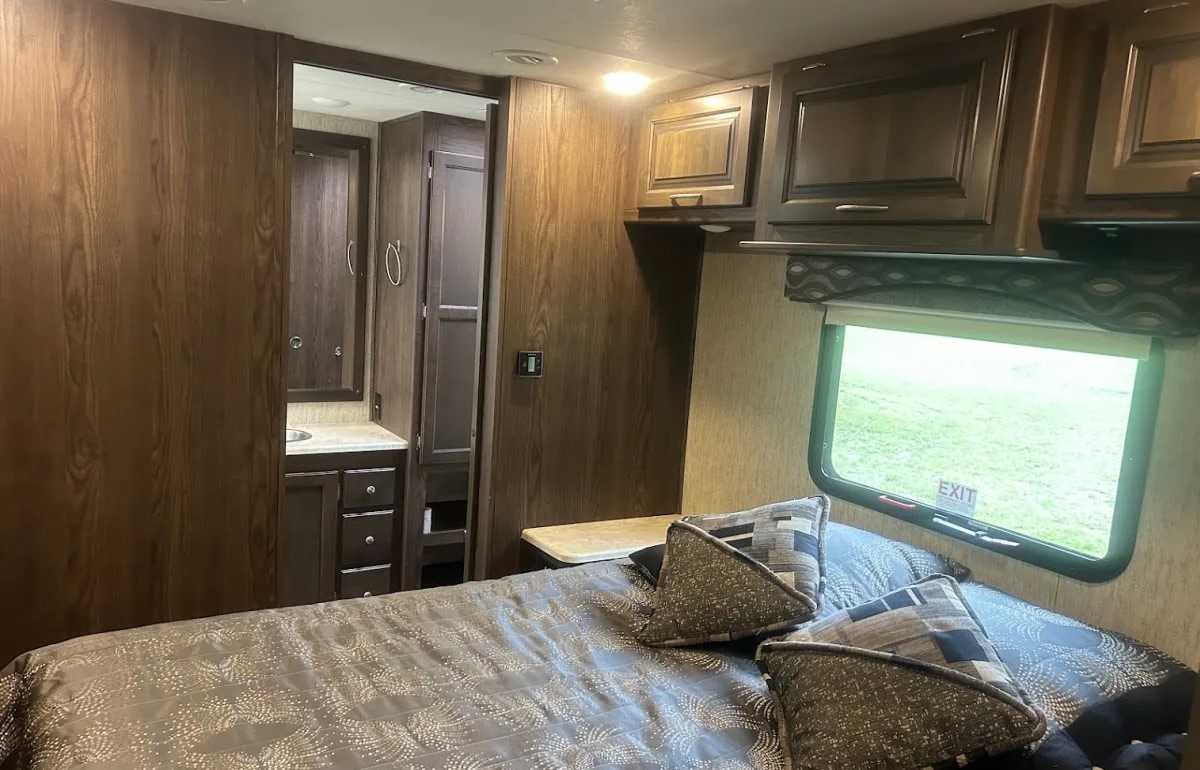 Comfortable RV rental interior, showcasing a cozy bedroom with a window view and an attached bathroom with storage.. Coachman Mirada 2018