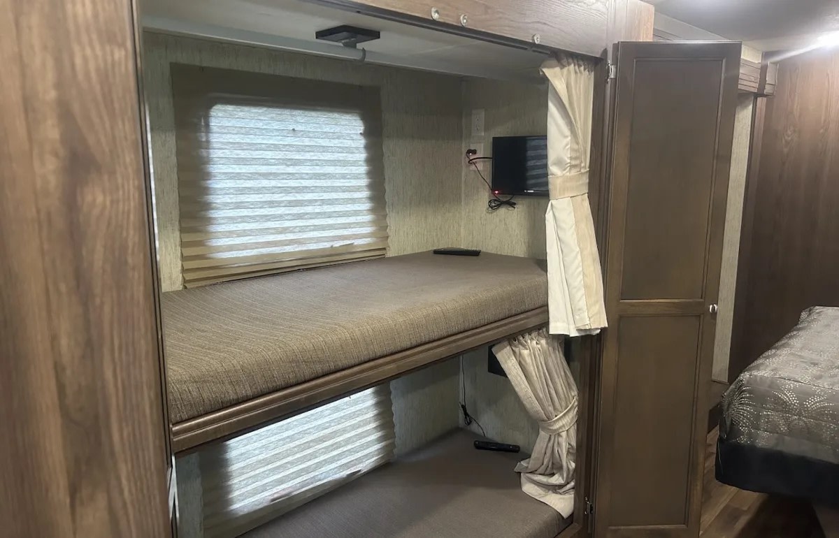 RV rental interior showcasing comfortable bunk beds, each with a TV and privacy blinds. Ideal sleeping space for travel.. Coachman Mirada 2018