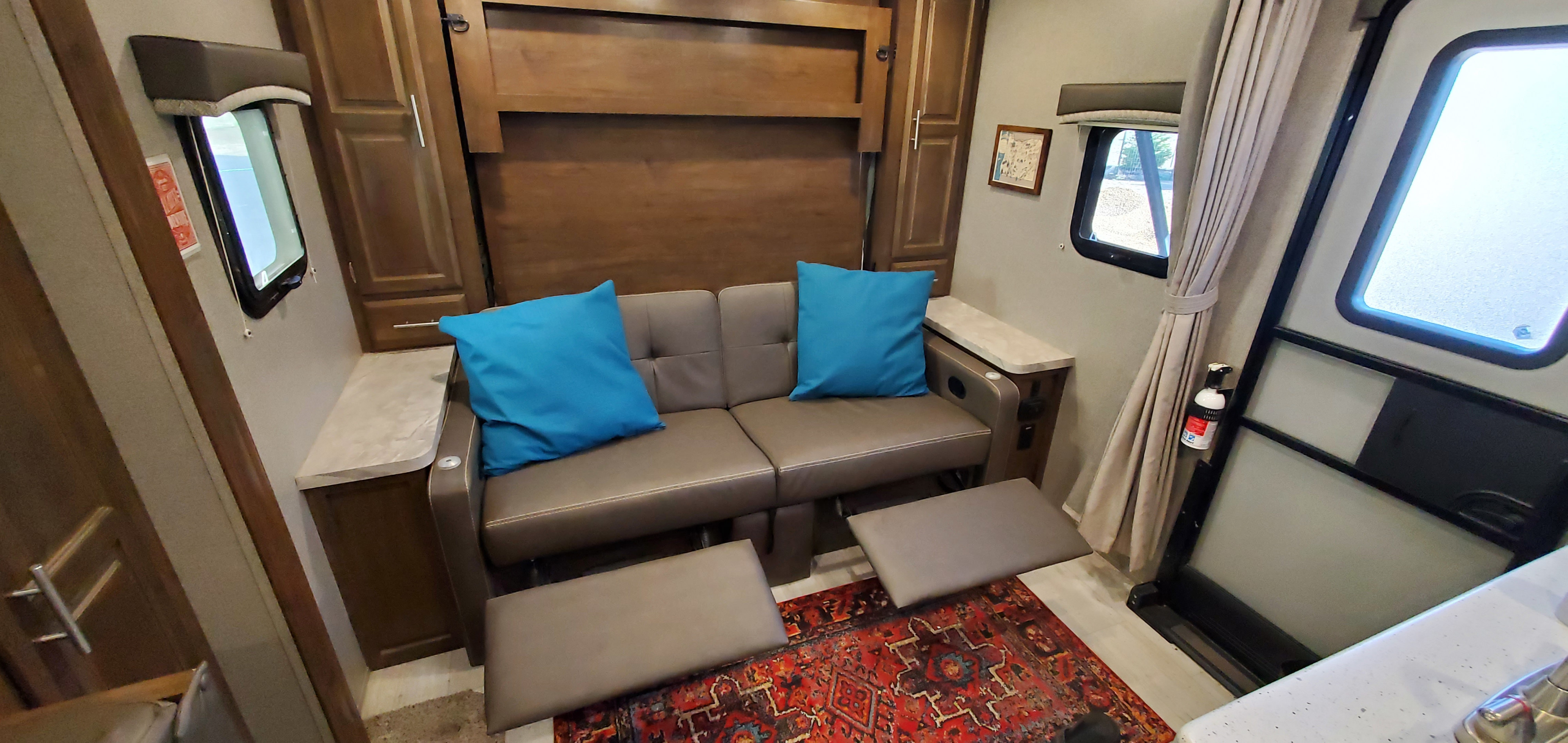 Cozy RV rental living space featuring a brown sofa, extended footrests, windows, and a colorful rug.. Forest River Rockwood Mini Lite 2019