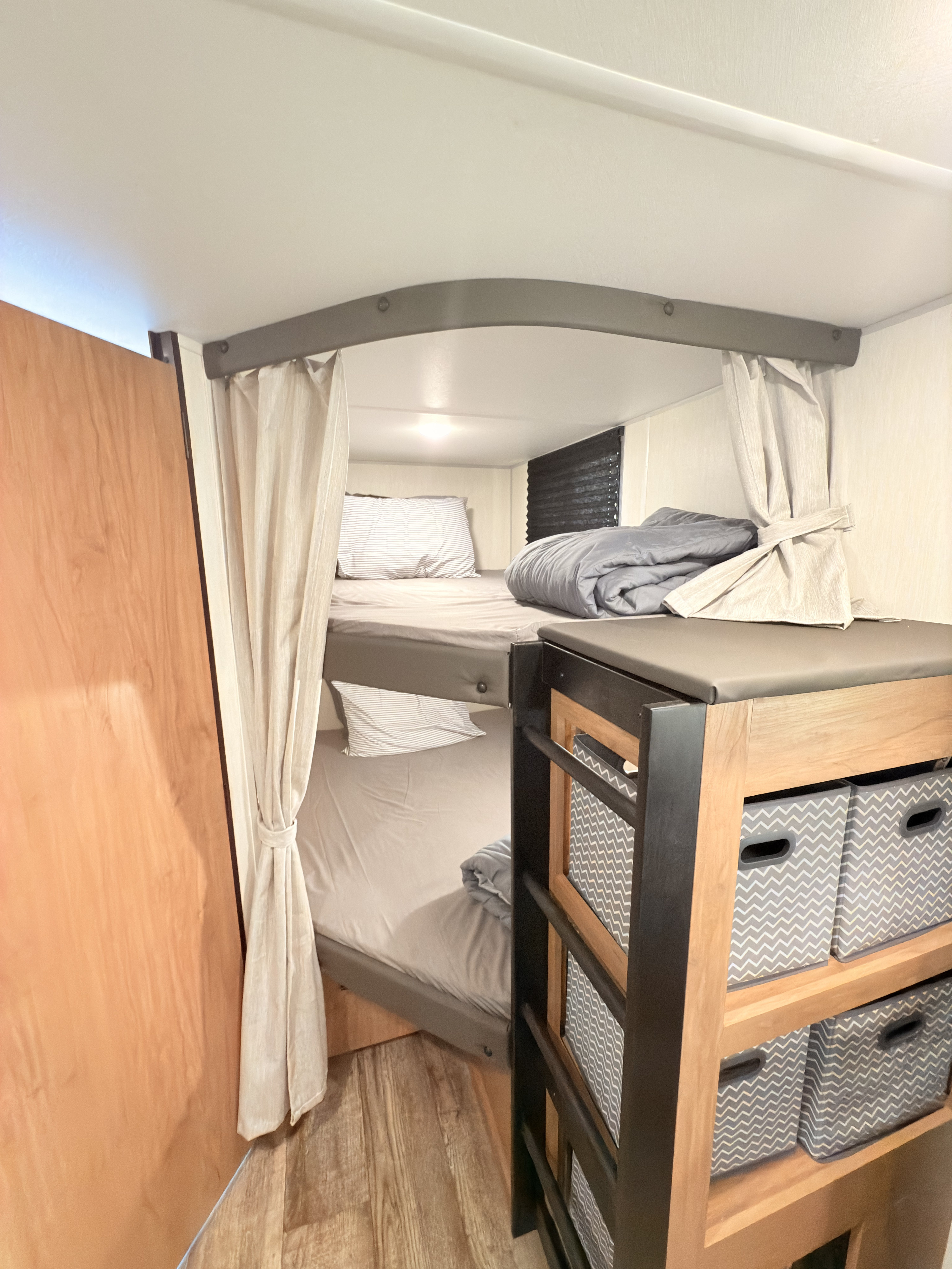Inside an RV rental: modern bunk beds with privacy curtains, built-in storage cubbies, and cozy bedding.. Forest River Campsite Reserve 26CJ 2025