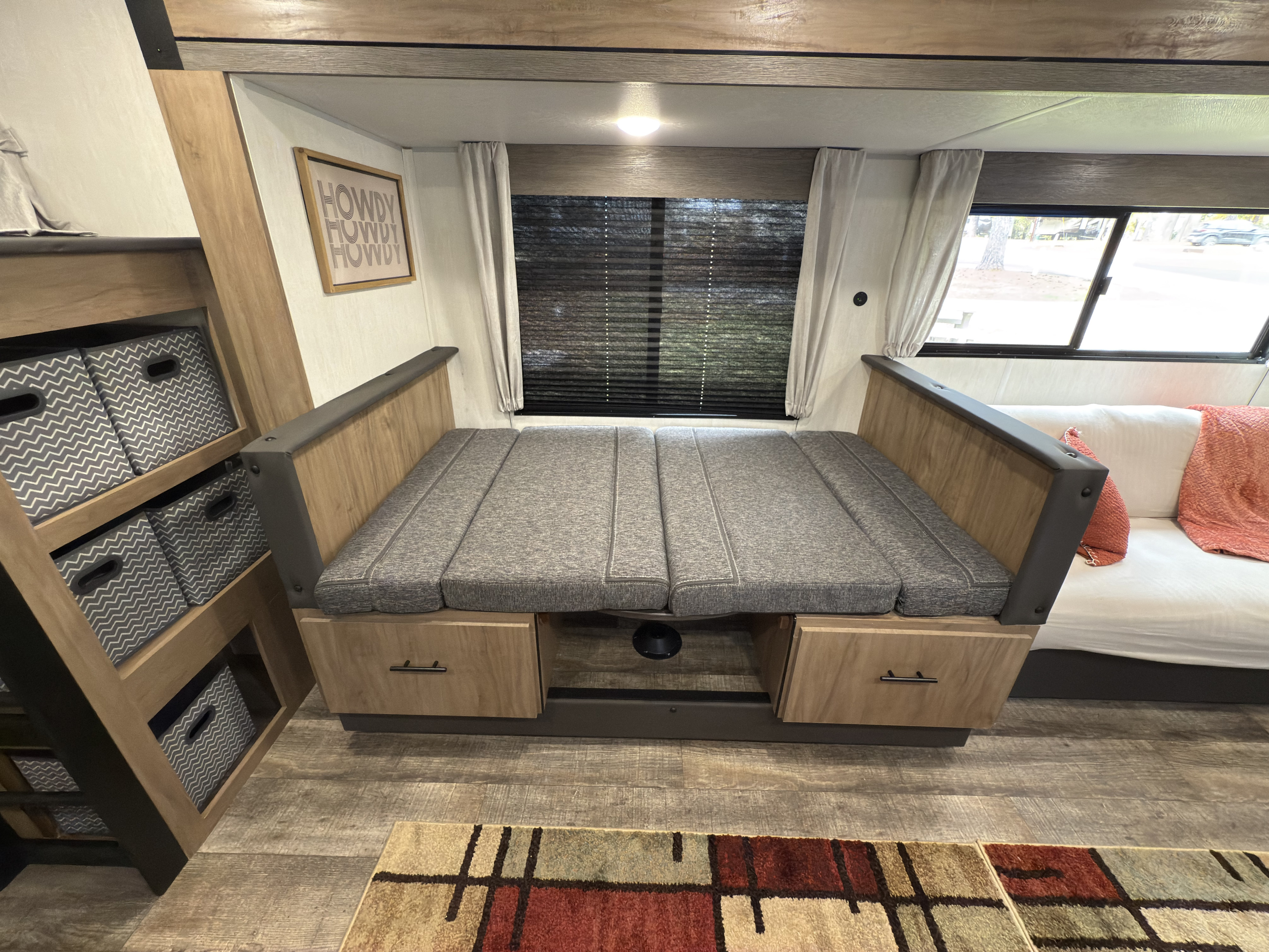 Cozy RV rental interior featuring a gray dinette that converts to a bed, with storage bins & a couch section visible.. Forest River Campsite Reserve 26CJ 2025
