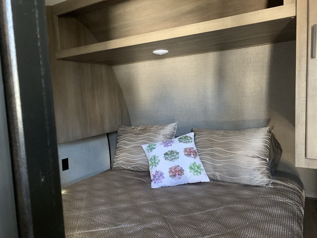 Comfortable RV rental bedroom featuring patterned bedding, overhead storage, and a light. A cozy sleeping area for your travels.. Starcraft Autumn Ridge 2024