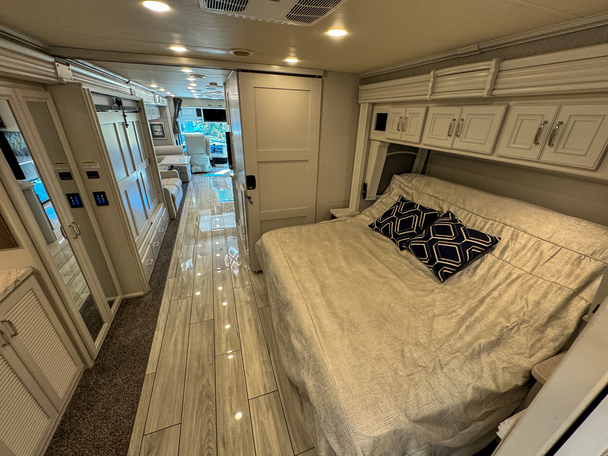 Spacious RV rental interior: bedroom with bed, overhead cabinets, and a hallway leading to the living area. Modern design.. Holiday Rambler Endeavor 2022