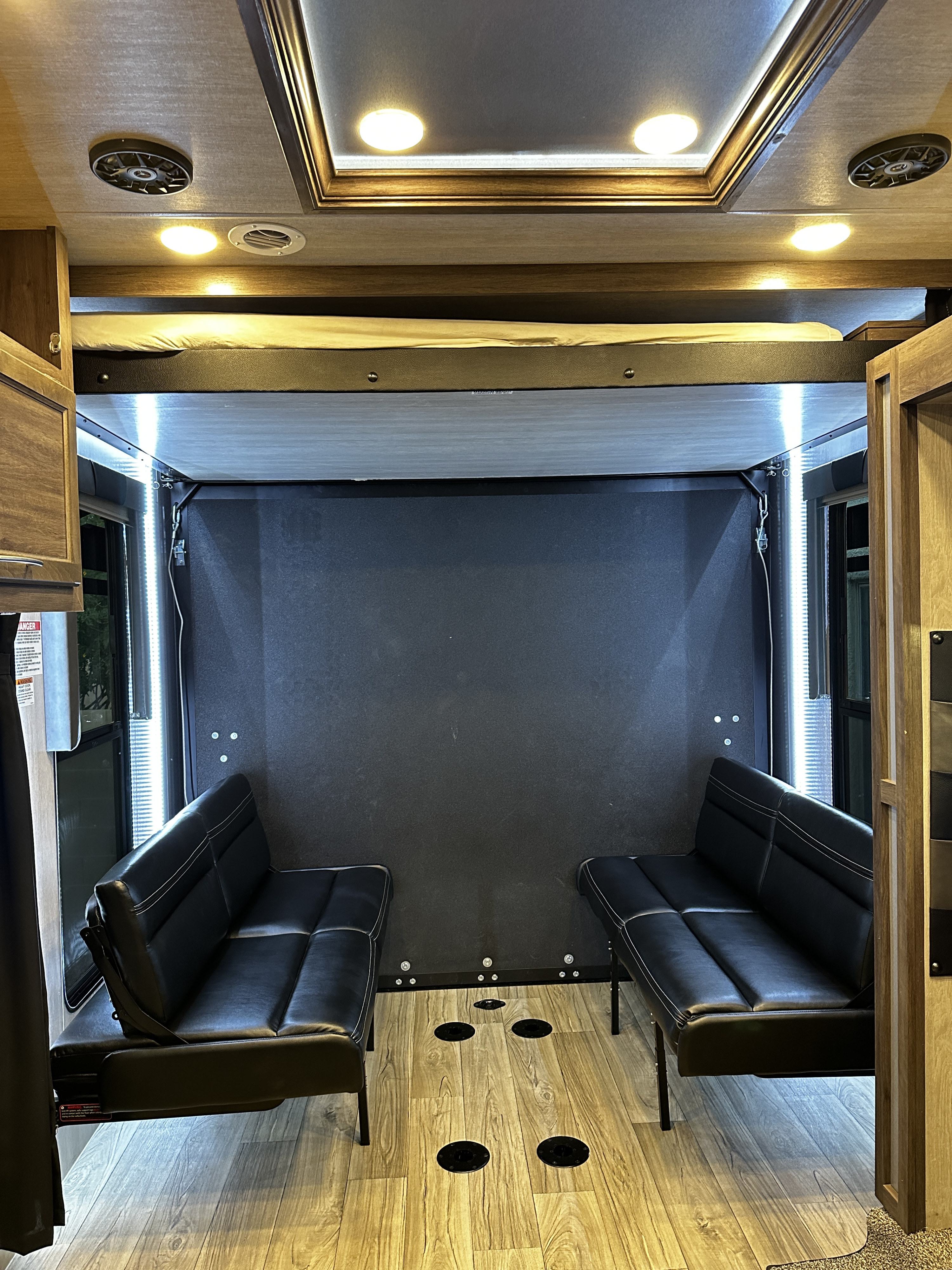 Inside an RV rental: versatile cargo area with twin sofas, an elevated bunk, and bright lighting on wood-look floors.. Genesis Supreme Rv Genesis Supreme 2023