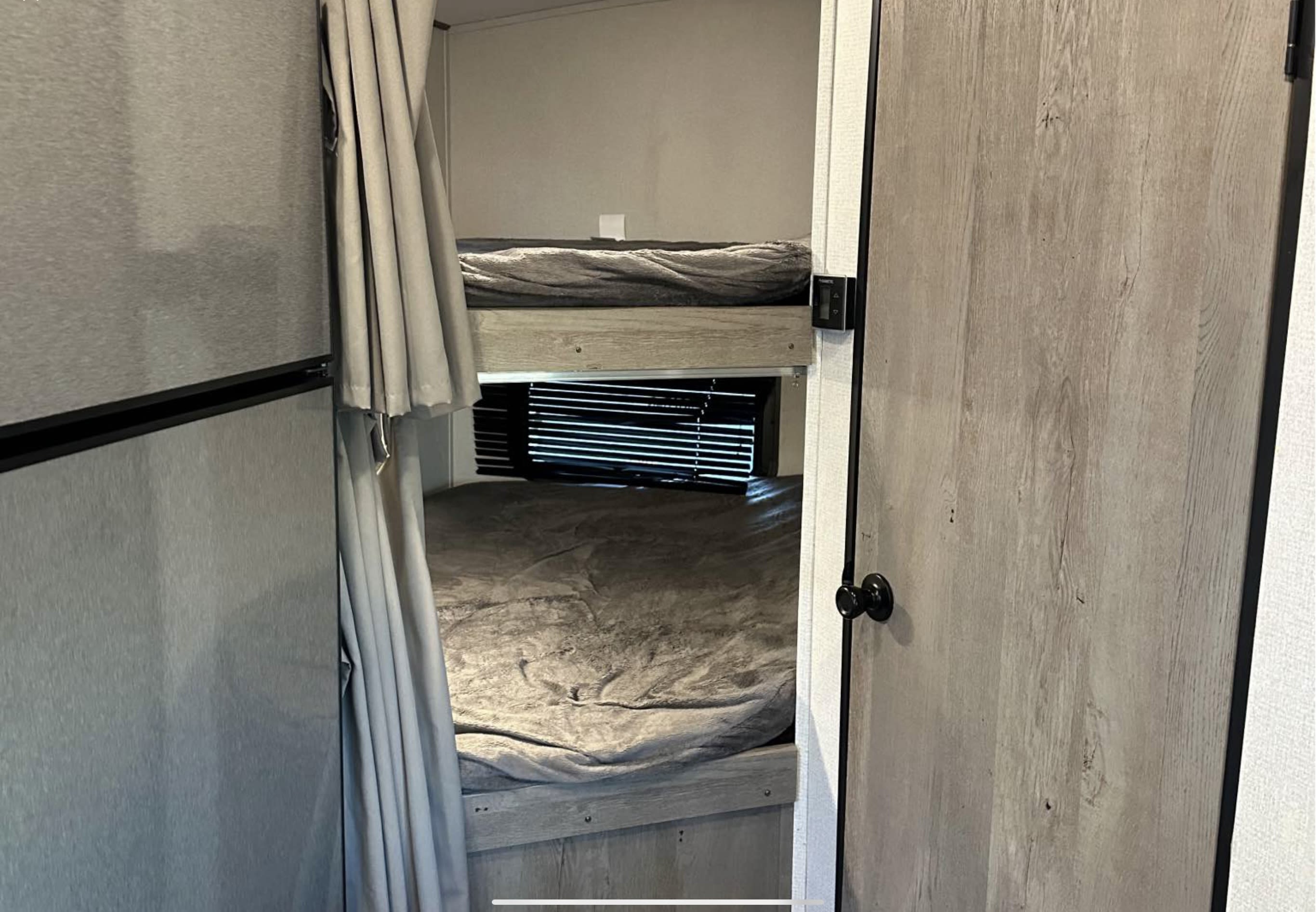 Cozy bunk beds in an rv rental, featuring soft grey bedding, privacy curtains, and window blinds.. Keystone springdale 220 2021
