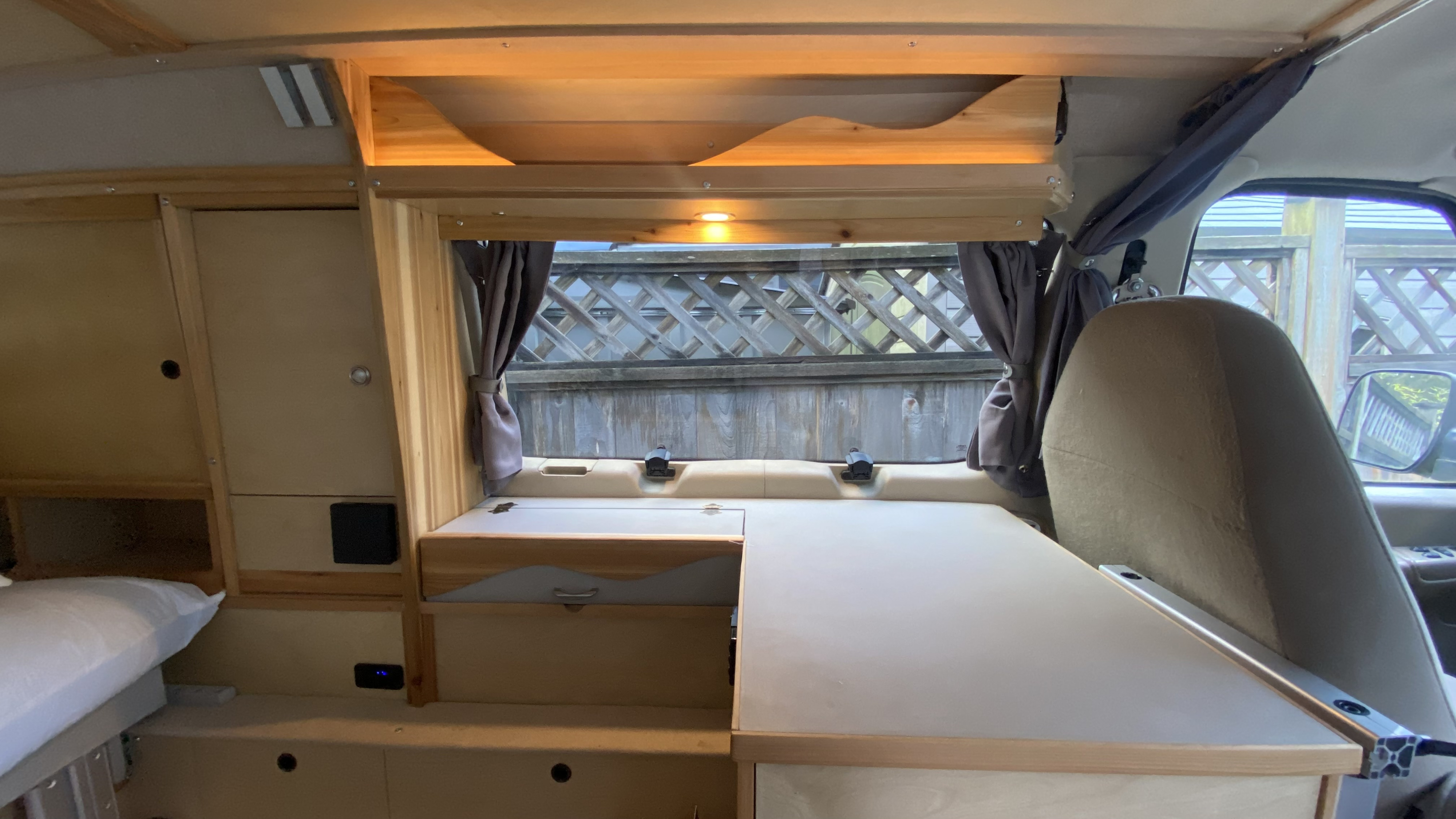 Custom wood interior of an RV rental van, featuring a cozy bed, counter space, and functional windows with curtains.. Ford Ford E350 2008